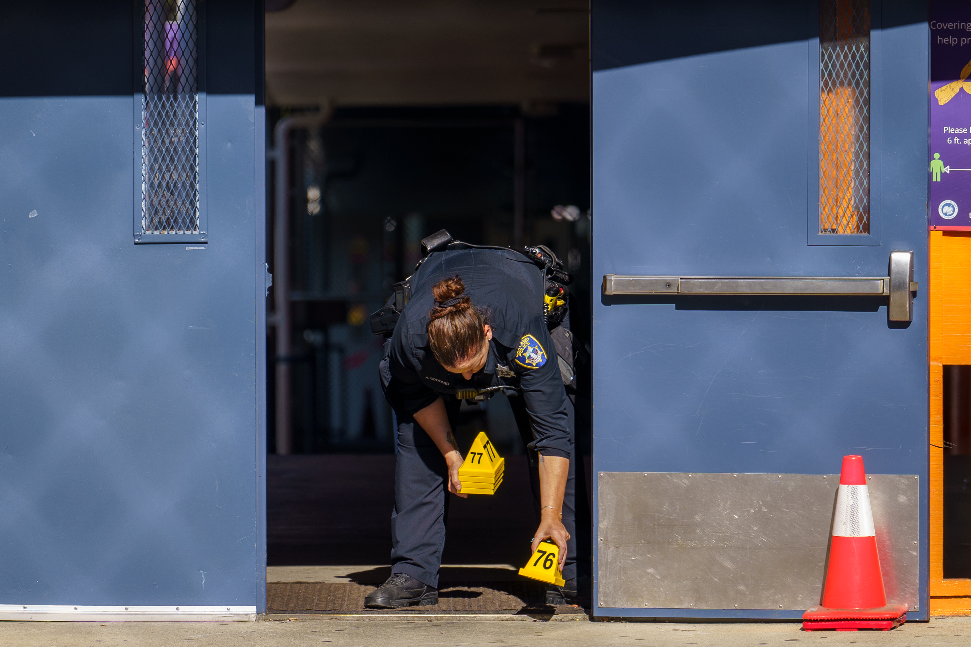 OAKLAND, CALIFORNIA - SEPTEMBER 28: Officer Astra Goddard drops an evidence marker near a back entrance to Bay Area Technology School following a multiple injury shooting in Oakland, Calif., on Wednesday, Sept. 28, 2022. (Dylan Bouscher/Bay Area News Group)