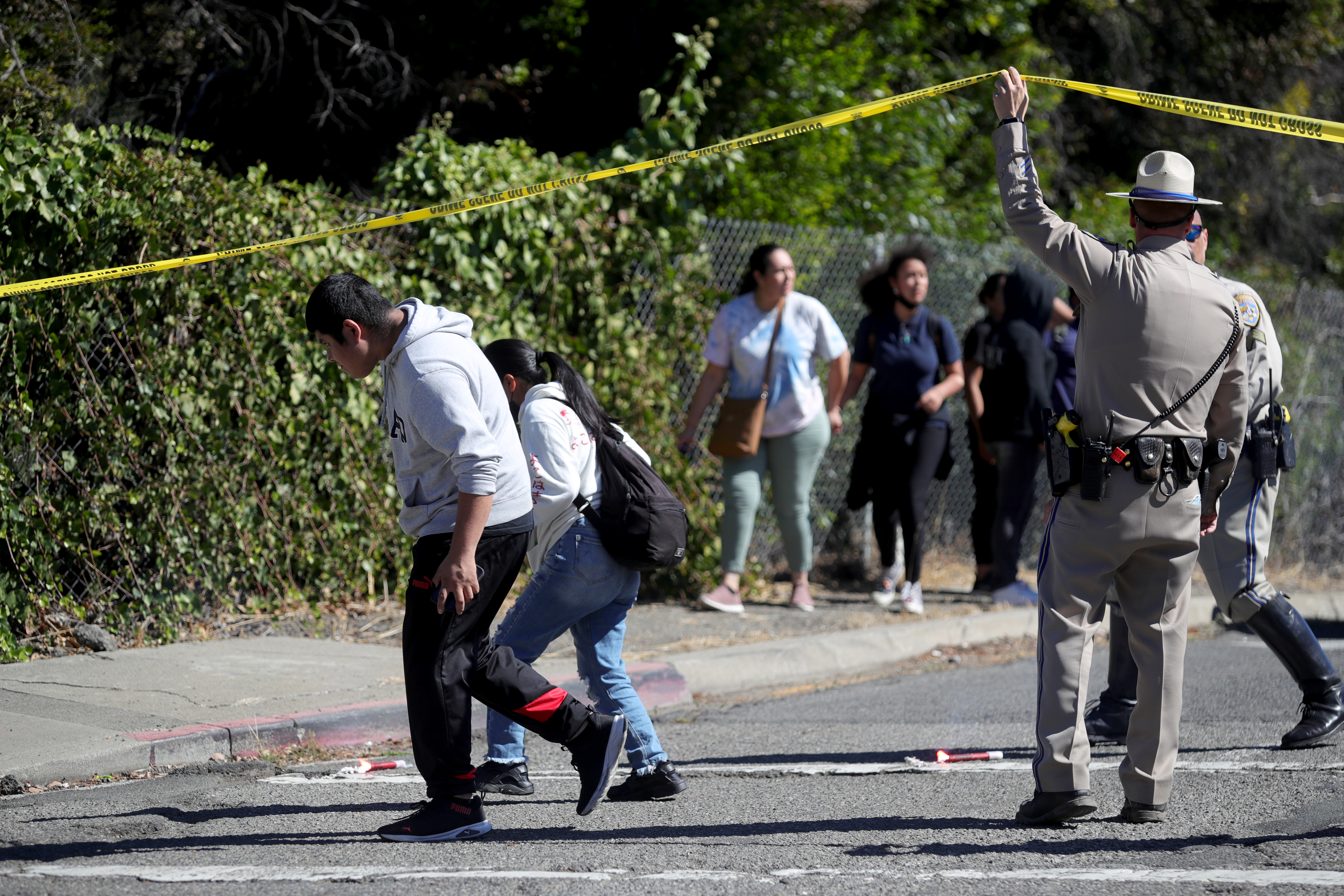 OAKLAND, CALIFORNIA - SEPTEMBER 28: A California Highway Patrol officer lifts the yellow tape to let parents and students leave the cordoned off area on Fontaine Street in Oakland, Calif., after a multiple people were shot in a complex of schools on Wednesday, Sept. 28, 2022. Ray Chavez/Bay Area News Group)