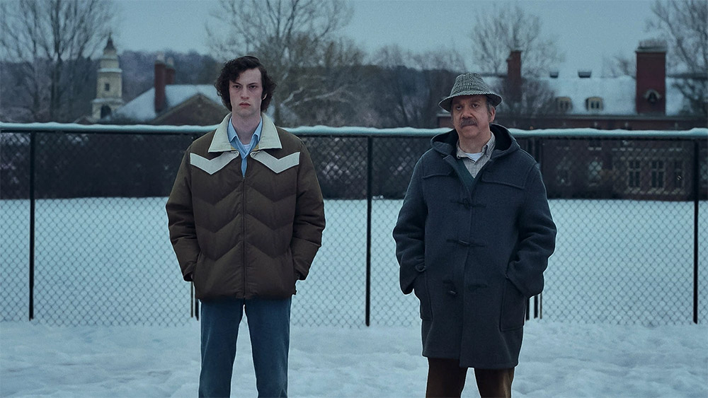 A young boy and older gentleman wearing a hat standing outside shoulder to shoulder in the snow