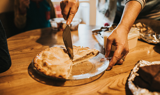 Hand holding a serving knife cuts in to a fresh, warm apple pie on a glass plate.
