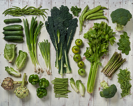 A selection of green vegetables arranged on a rustic white wooden table.