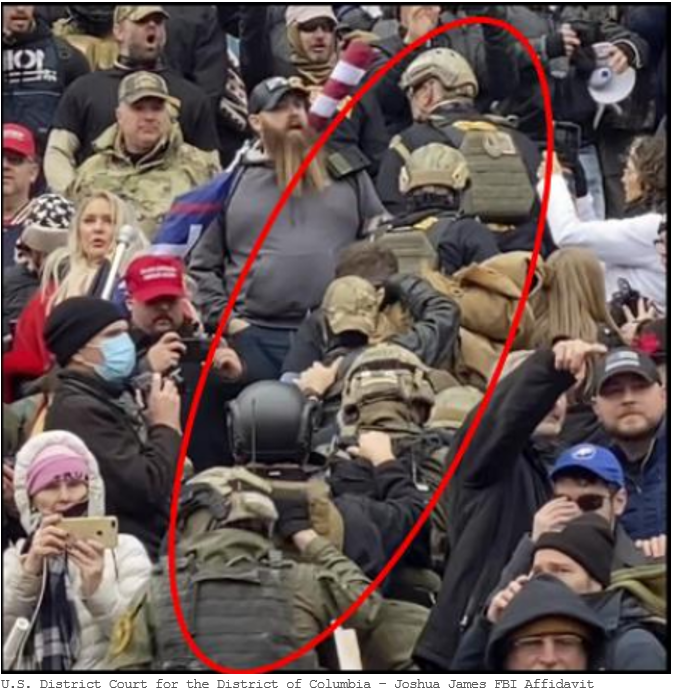 A militia walks in single file through the crowd during the January 6th attack. They wear helmets and combat gear.