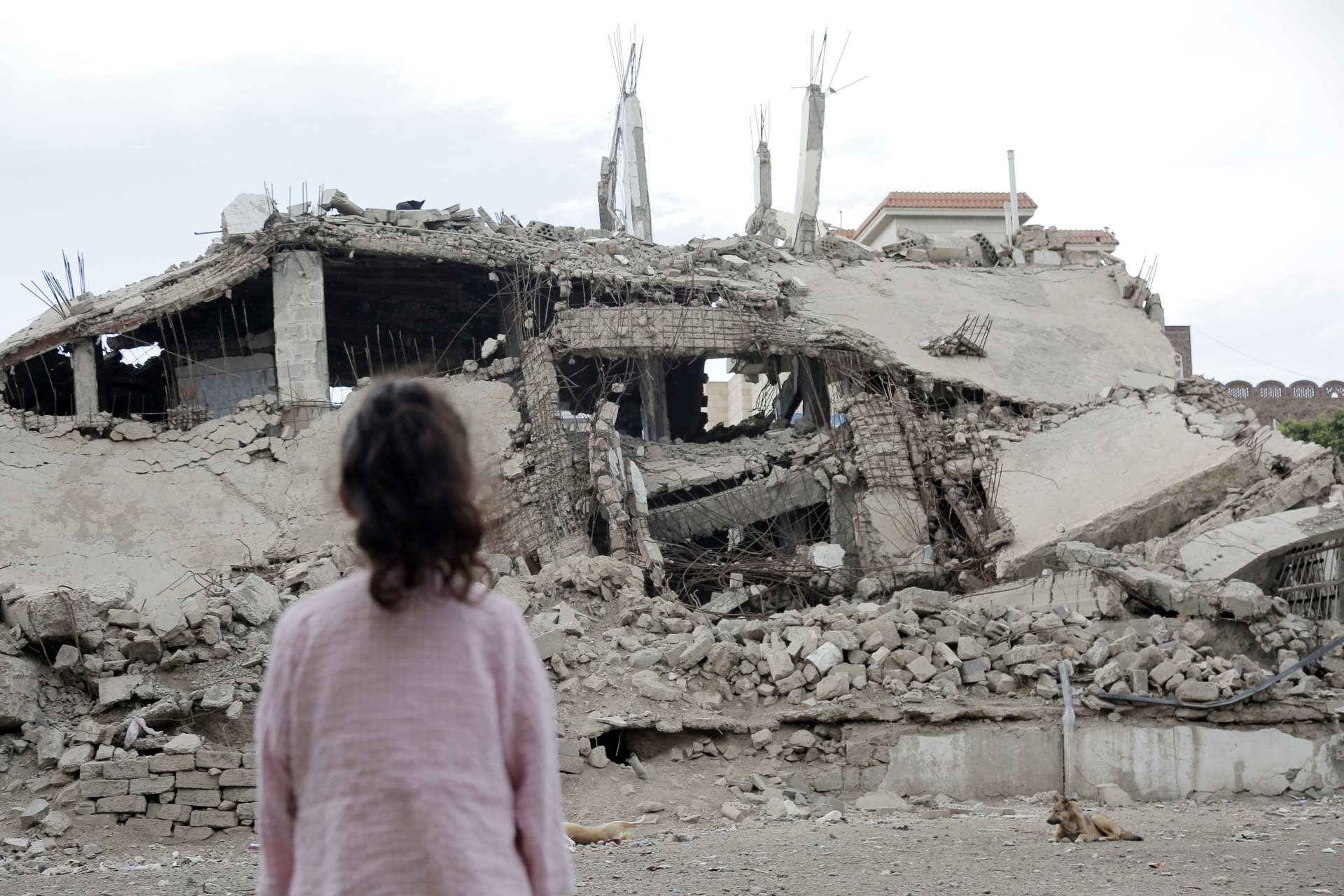 A girl looks at a building destroyed by aerial attacks carried out by warplanes