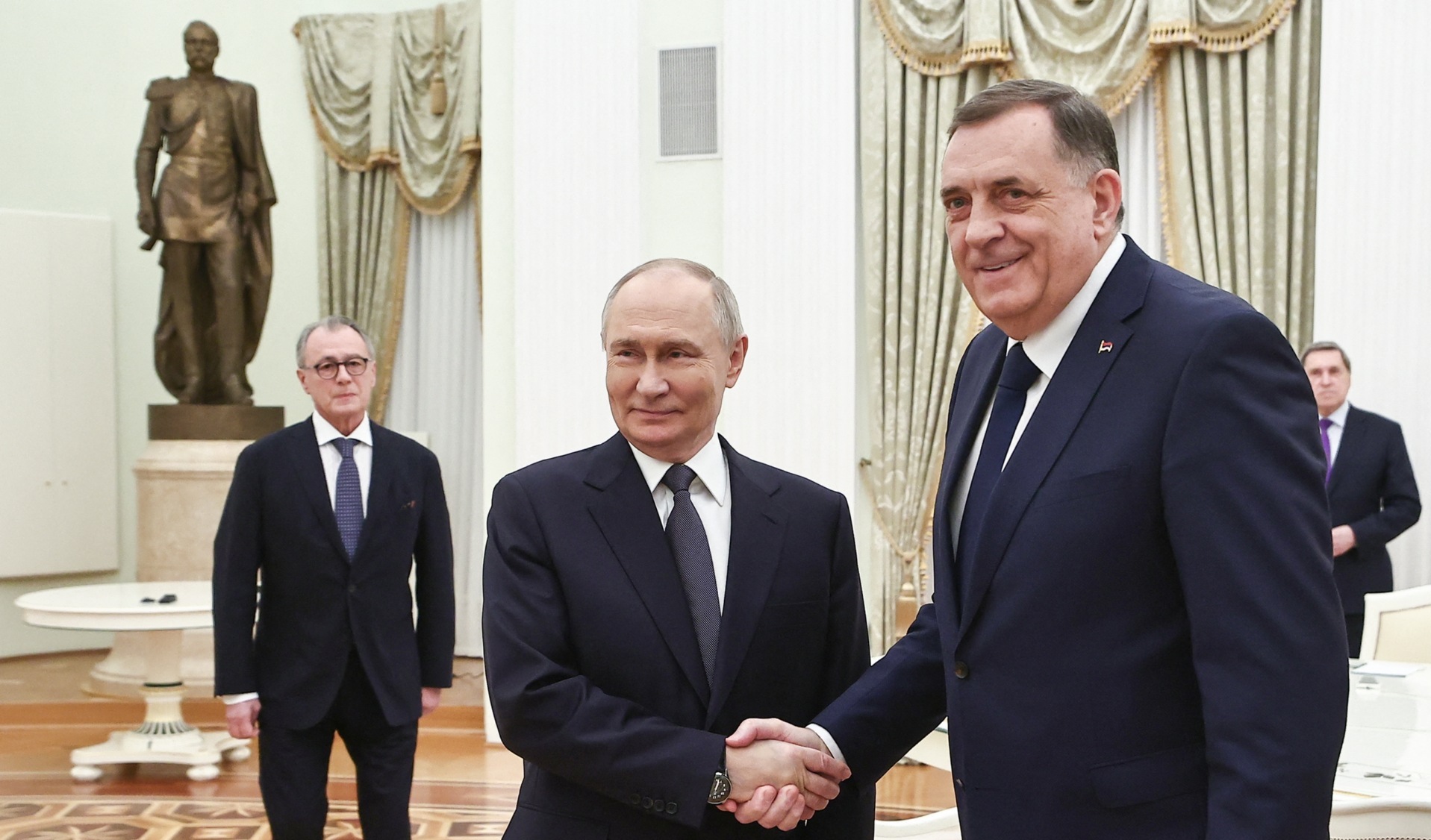 Dodik, at right, shakes hands with Putin to the left, with another figure in the back left of the frame, in an ornately decorated room.