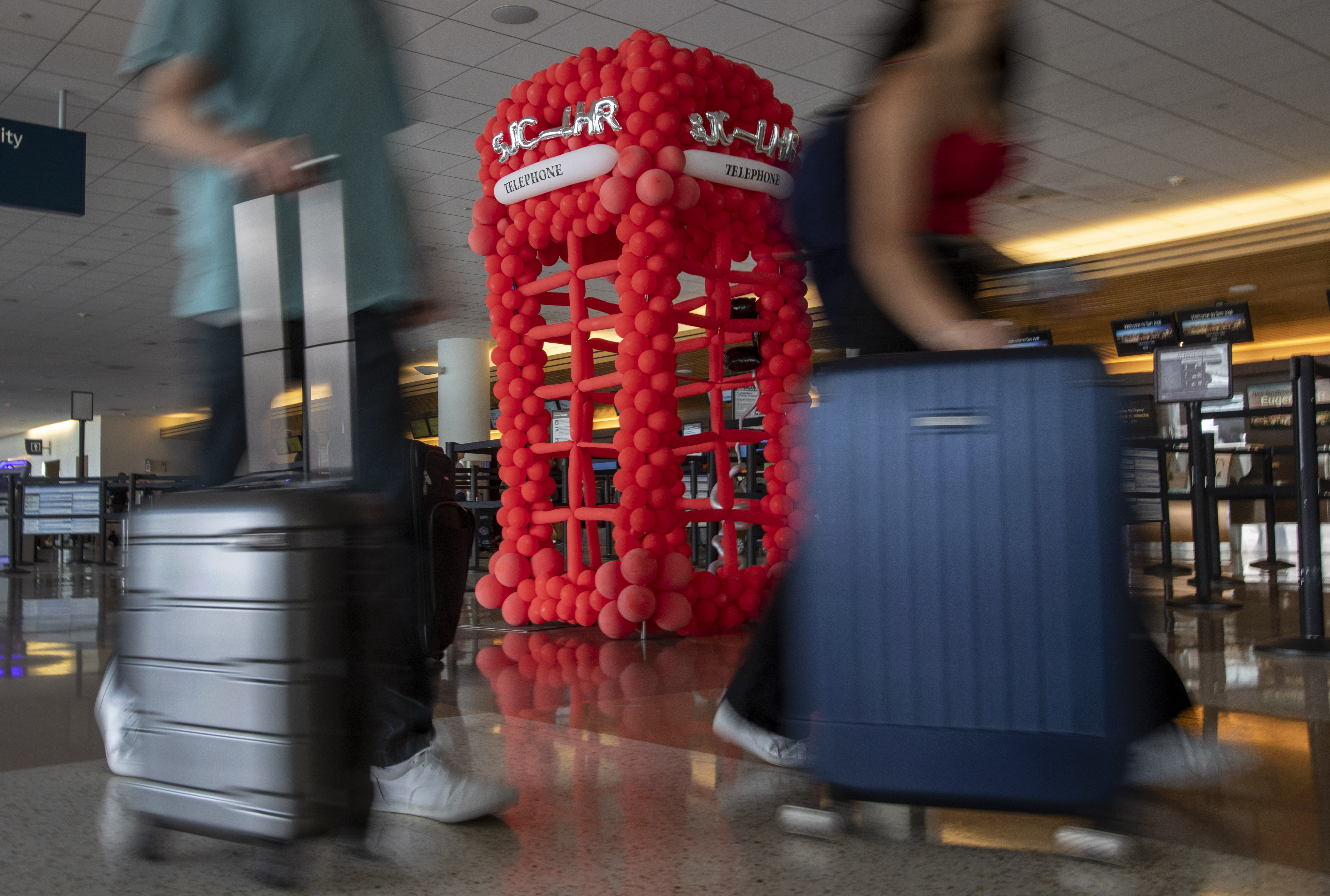 Airline passengers rush past a balloon sculpture of a British phone booth at Mineta San Jose International Airport