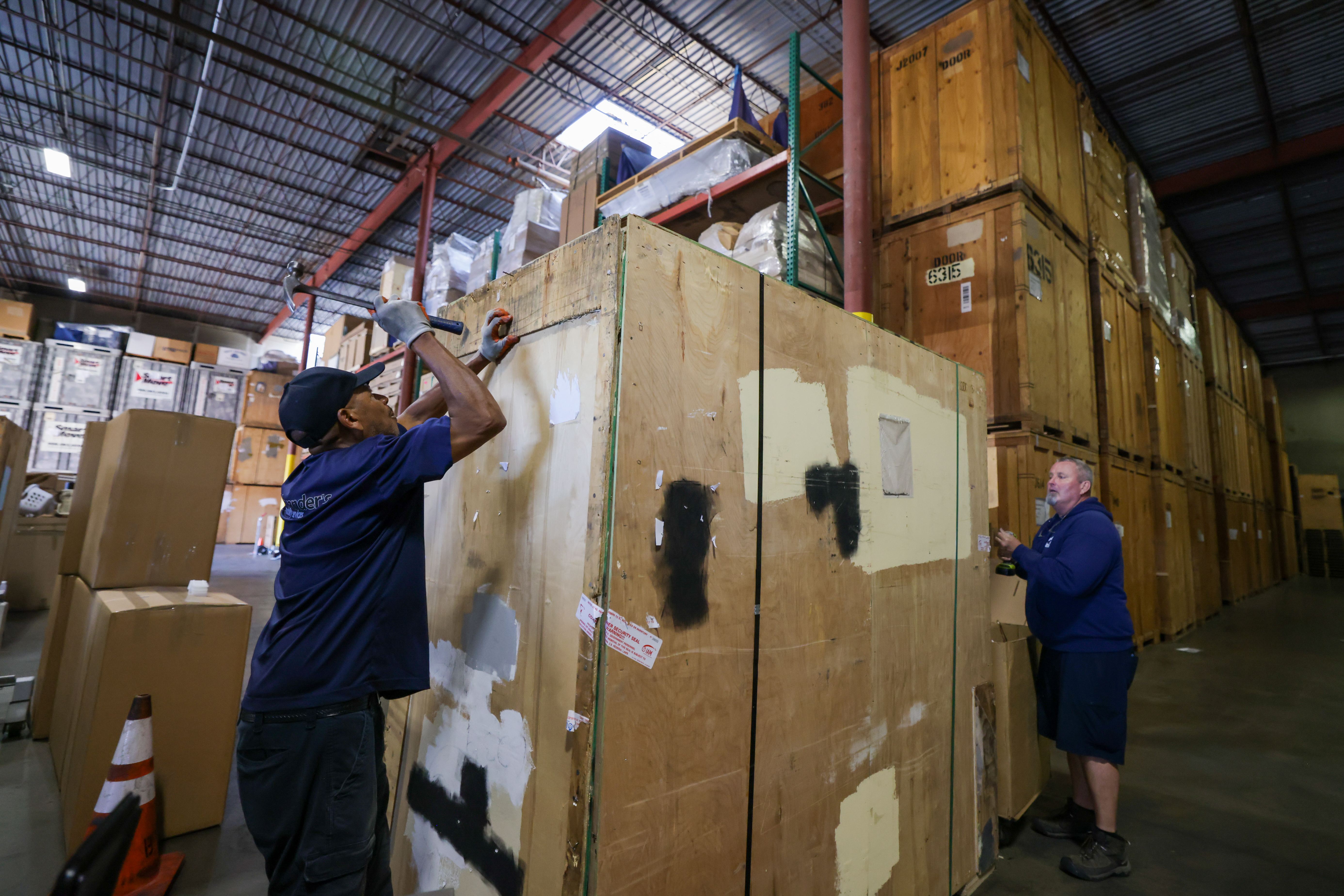 HAYWARD, CALIFORNIA - JULY 15: Warehouse manager Winford Talford, left, and Mark Macy, owner of Macy Movers, seal a wooden box after filling it with customers' belongings at the Macy Movers warehouse in Hayward, Calif., on Friday, July 15, 2022. Thirty percent of the containers storing clients' belongings are waiting to be shipped out of state, mostly to Tennessee and Texas, Mark said. (Ray Chavez/Bay Area News Group)