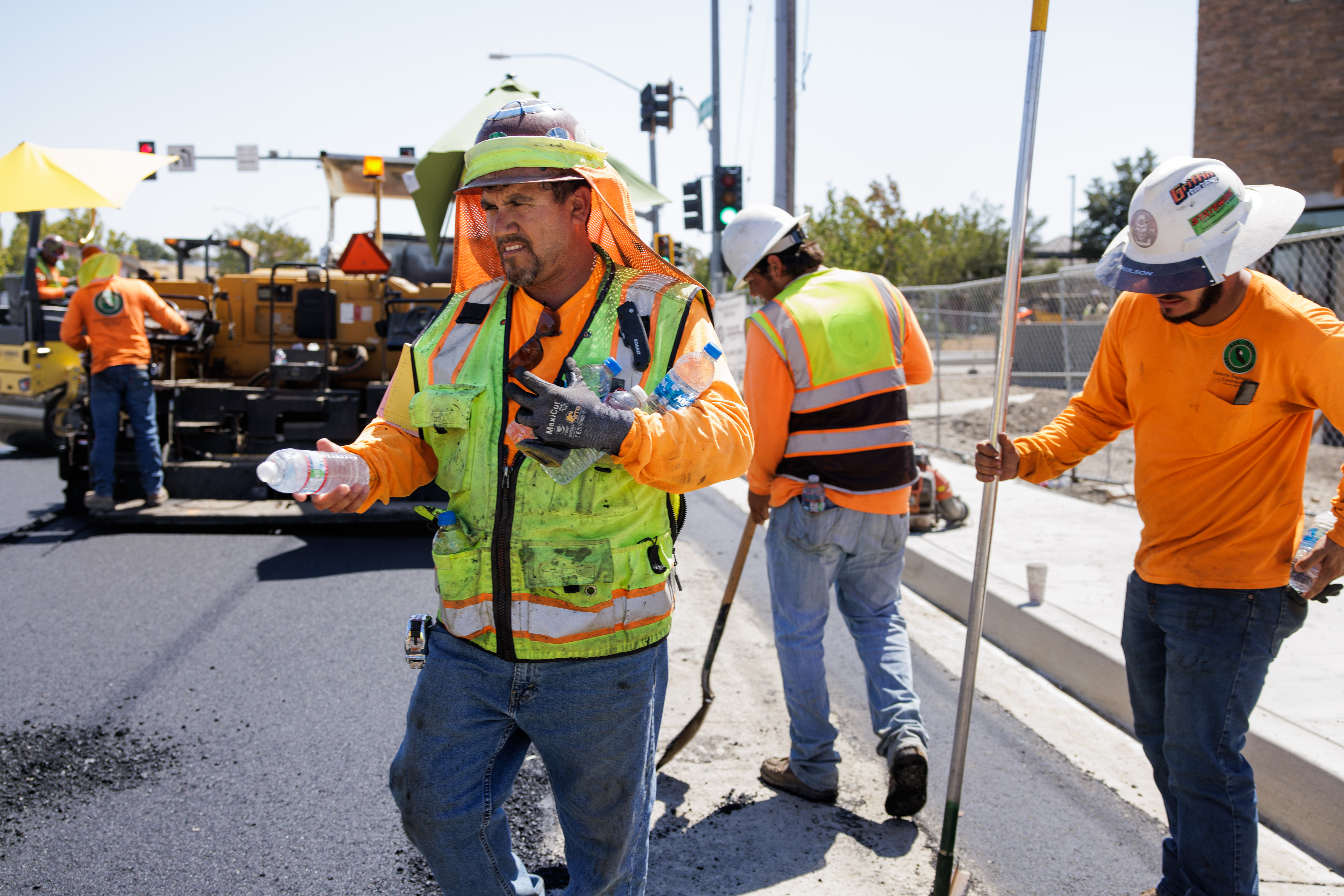 With temperatures over 100 degrees, construction worker Margarito Vargas from Eleven Western Builders gives fellow workers water bottles while paving a road in Livermore, Calif., on Aug. 16, 2022. The road work is part of a new Chick-fil-A restaurant location. (Dai Sugano/Bay Area News Group)