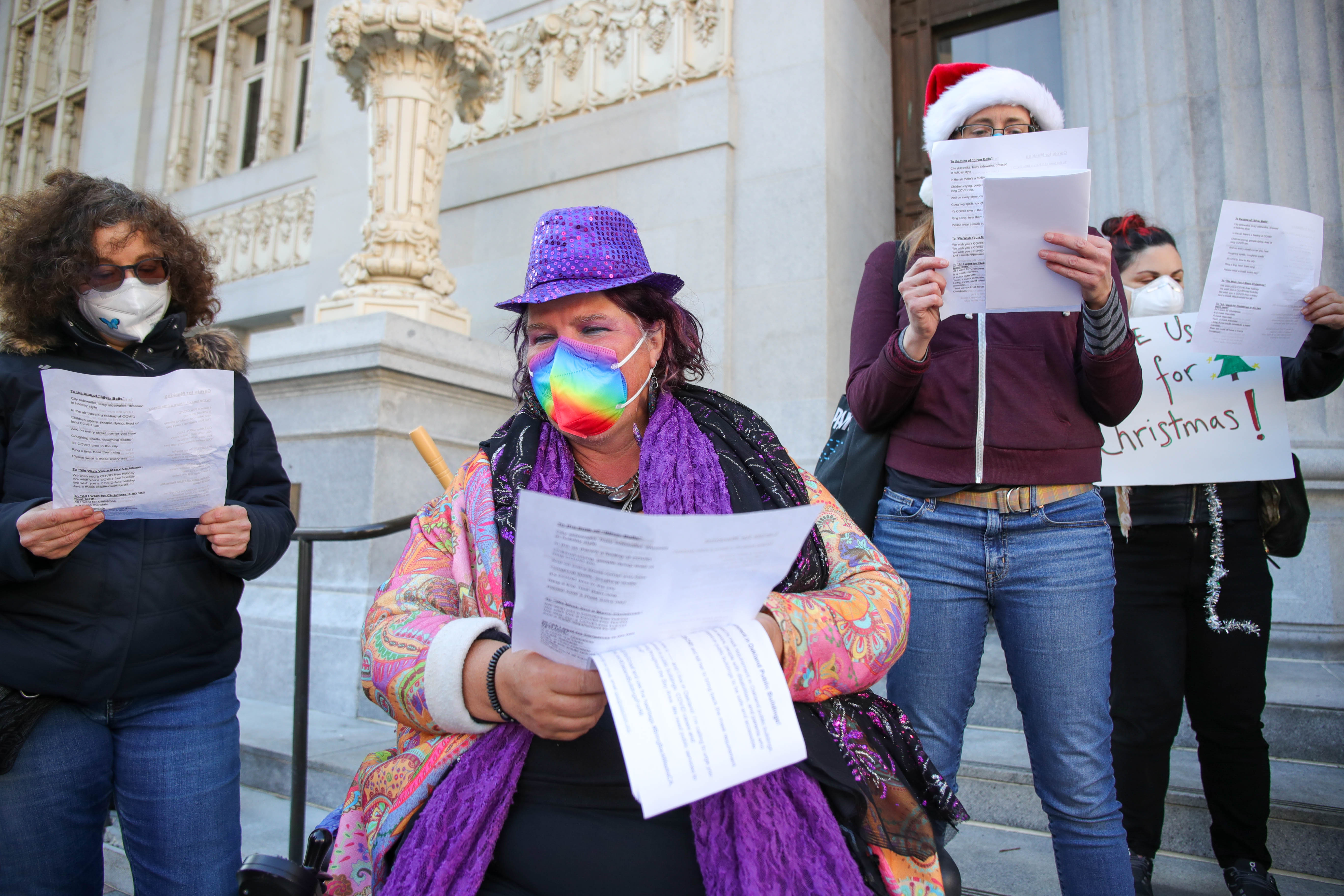 Maya Scott-Chung, center, of Emeryville, and members of Center for Independent Living, Senior and Disability Action, and Marked by COVID sing carols outside Oakland City Hall in Oakland, Calif., on Tuesday, Dec. 13, 2022.