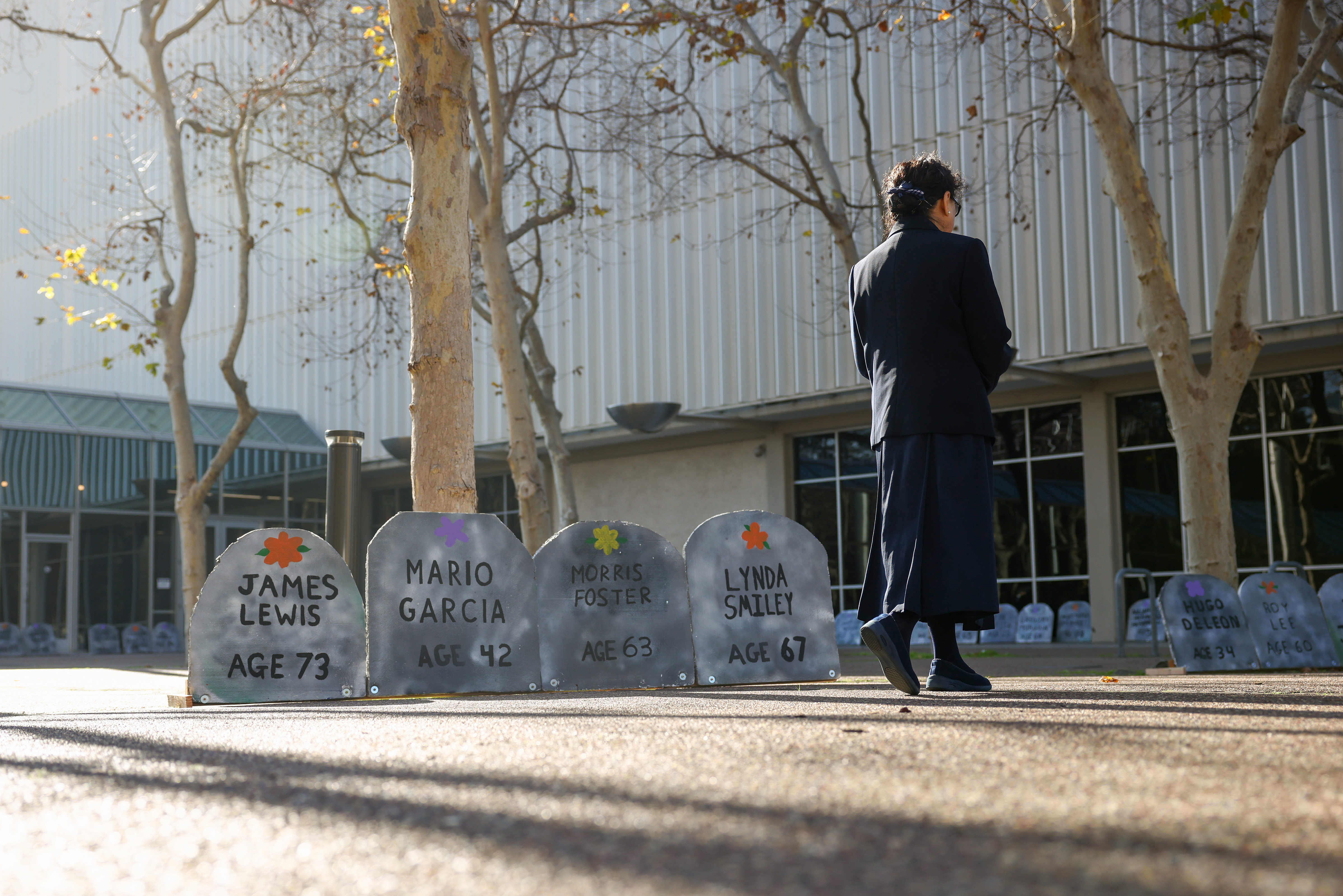 A woman walks past tombstones during an annual memorial for all unhoused people who died over the past year at the Santa Clara County building in San Jose, Calif., on Wednesday, Dec. 21, 2022. (Shae Hammond/Bay Area News Group)
