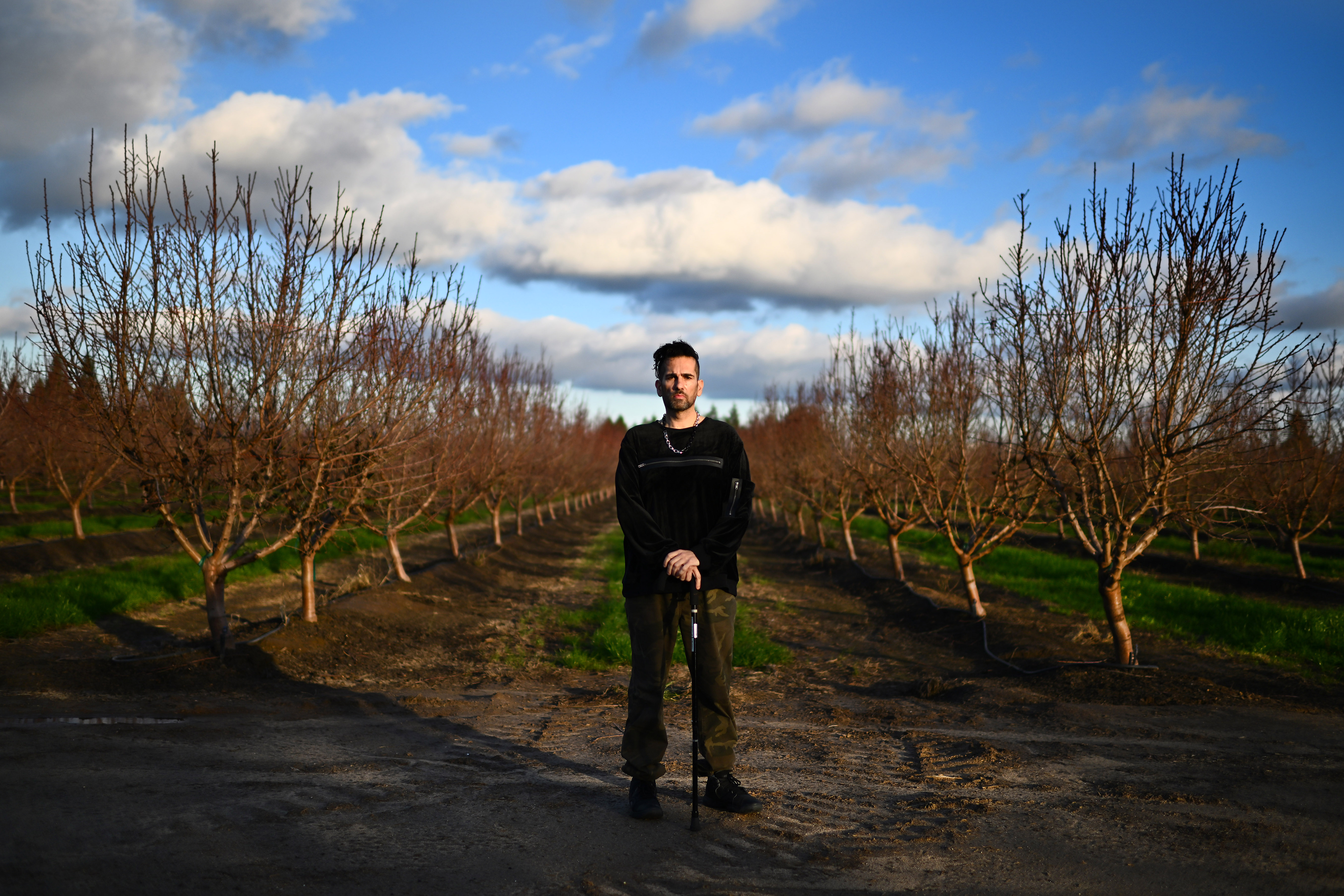 Jaime Gonzalez, 48, of Modesto, is photographed in front of an almond orchard in Modesto, Calif., on Thursday, Jan. 19, 2023. A decade and a half ago, as Gonzalez walked out of a Modesto hospital after a month of treatment for a blood clot, a dust storm kicked up, wafting fungal spores into his lungs, giving him Valley fever. Gonzalez uses a cane to help him walk after suffering his 14th blood clot since getting Valley Fever. He also suffers from balance issues and is immune compromised. (Jose Carlos Fajardo/Bay Area News Group)