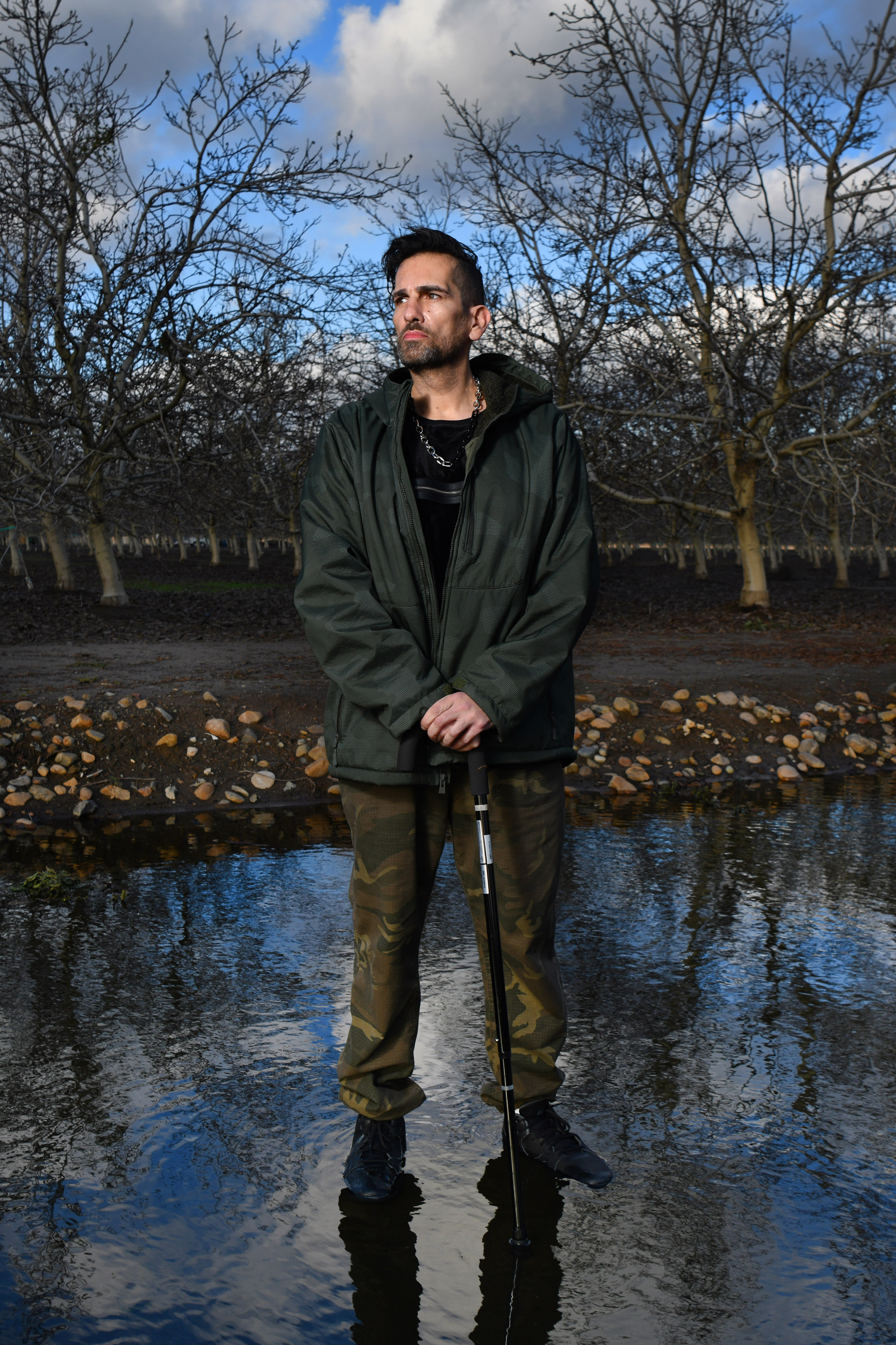 Jaime Gonzalez, 48, of Modesto, is photographed in front of a walnut orchard in Modesto, Calif., on Thursday, Jan. 19, 2023. A decade and a half ago, as Gonzalez walked out of a Modesto hospital after a month of treatment for a blood clot, a dust storm kicked up, wafting fungal spores into his lungs, giving him Valley fever. Gonzalez uses a cane to help him walk after suffering his 14th blood clot since getting Valley Fever. He also suffers from balance issues and is immune compromised. (Jose Carlos Fajardo/Bay Area News Group)