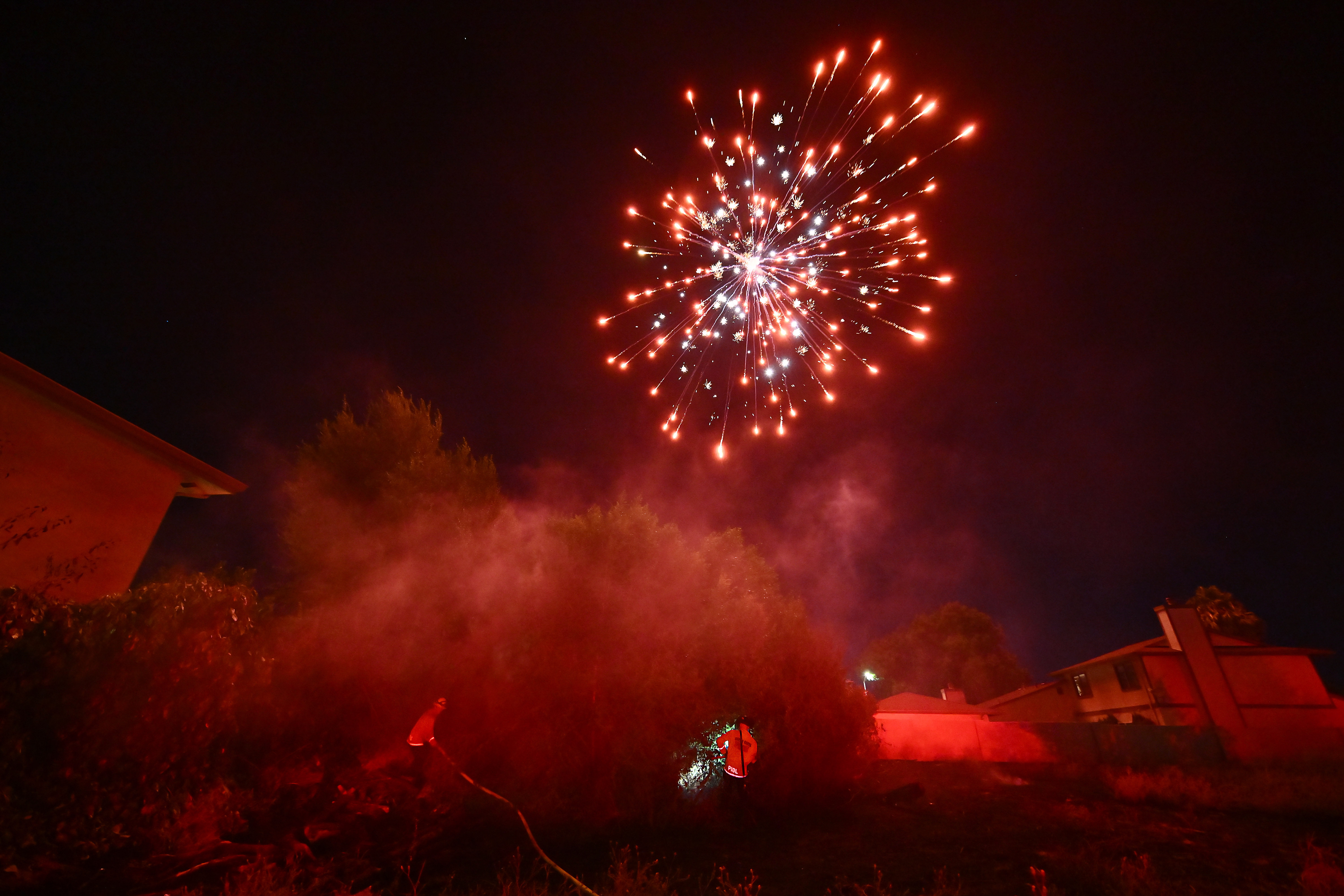 An illegal firework explodes above the heads of Contra Costa Firefighters as they finish extinguishing a vegetation fire caused by illegal fireworks during Fourth of July celebrations in Antioch, Calif., on Thursday, July 4, 2024. The vegetation fire was at the corner of Sycamore Drive and L Street. (Jose Carlos Fajardo/Bay Area News Group)