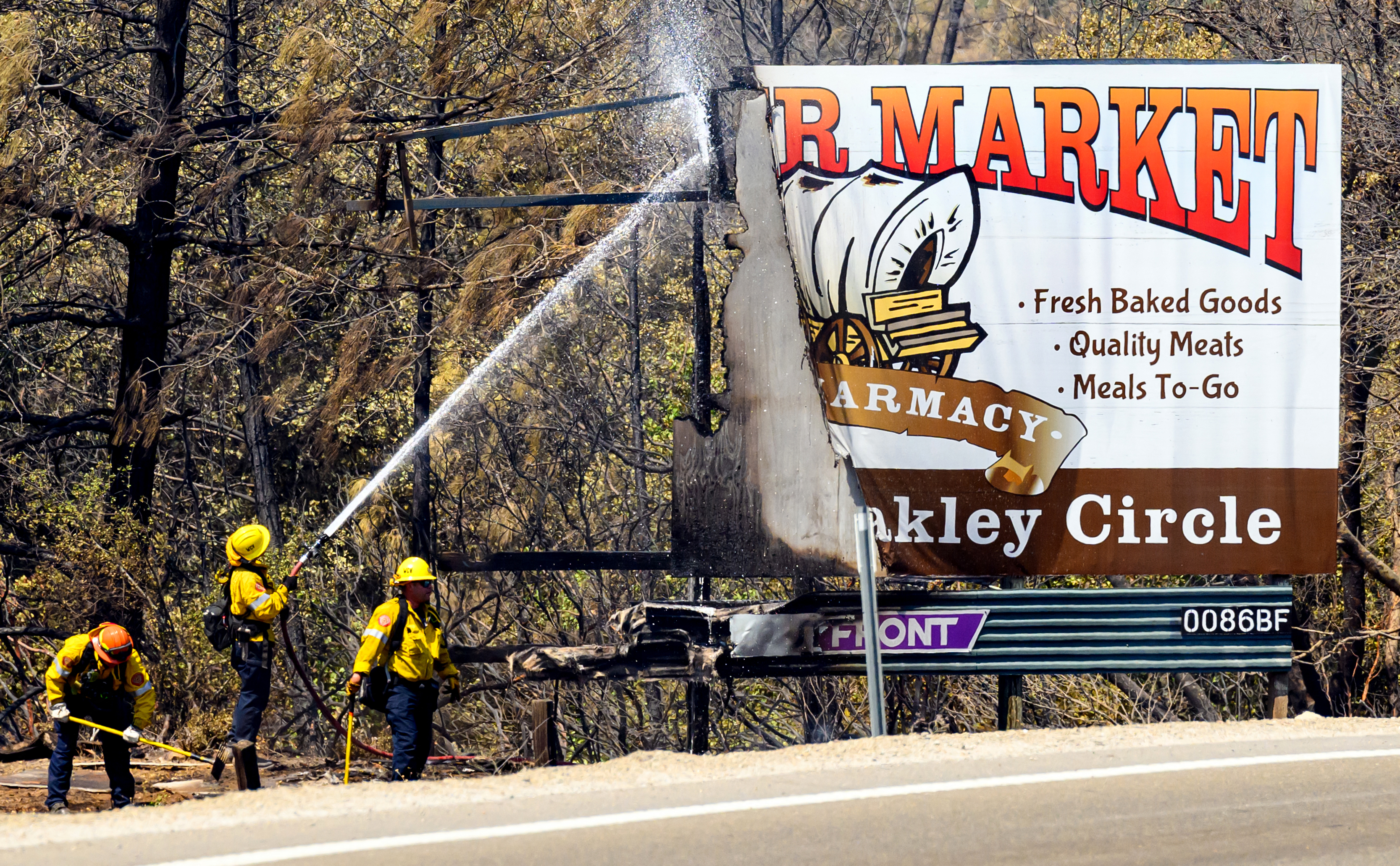 Firefighters extinguish a burning billboard during the French Fire in Mariposa, California, on July 5, 2024. The wildfire shut down the main highway to Yosemite National Park as red flag fire warnings and high temperatures continue throughout the state. (Photo by JOSH EDELSON / AFP) (Photo by JOSH EDELSON/AFP via Getty Images)