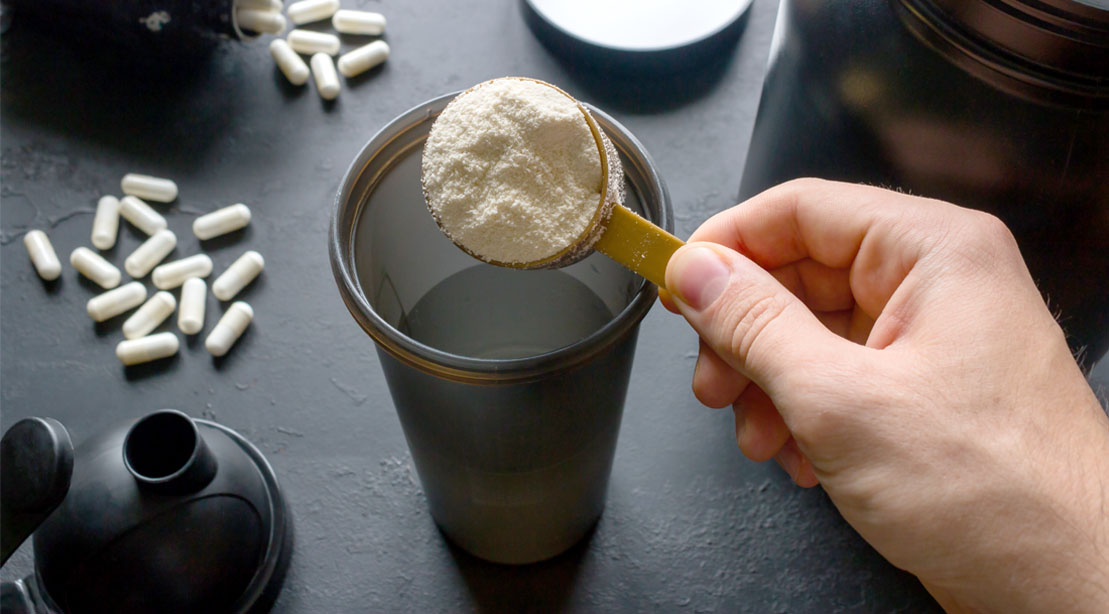 Protein powder and BCAAs powder in a scooper being poured into a protein shaker bottle