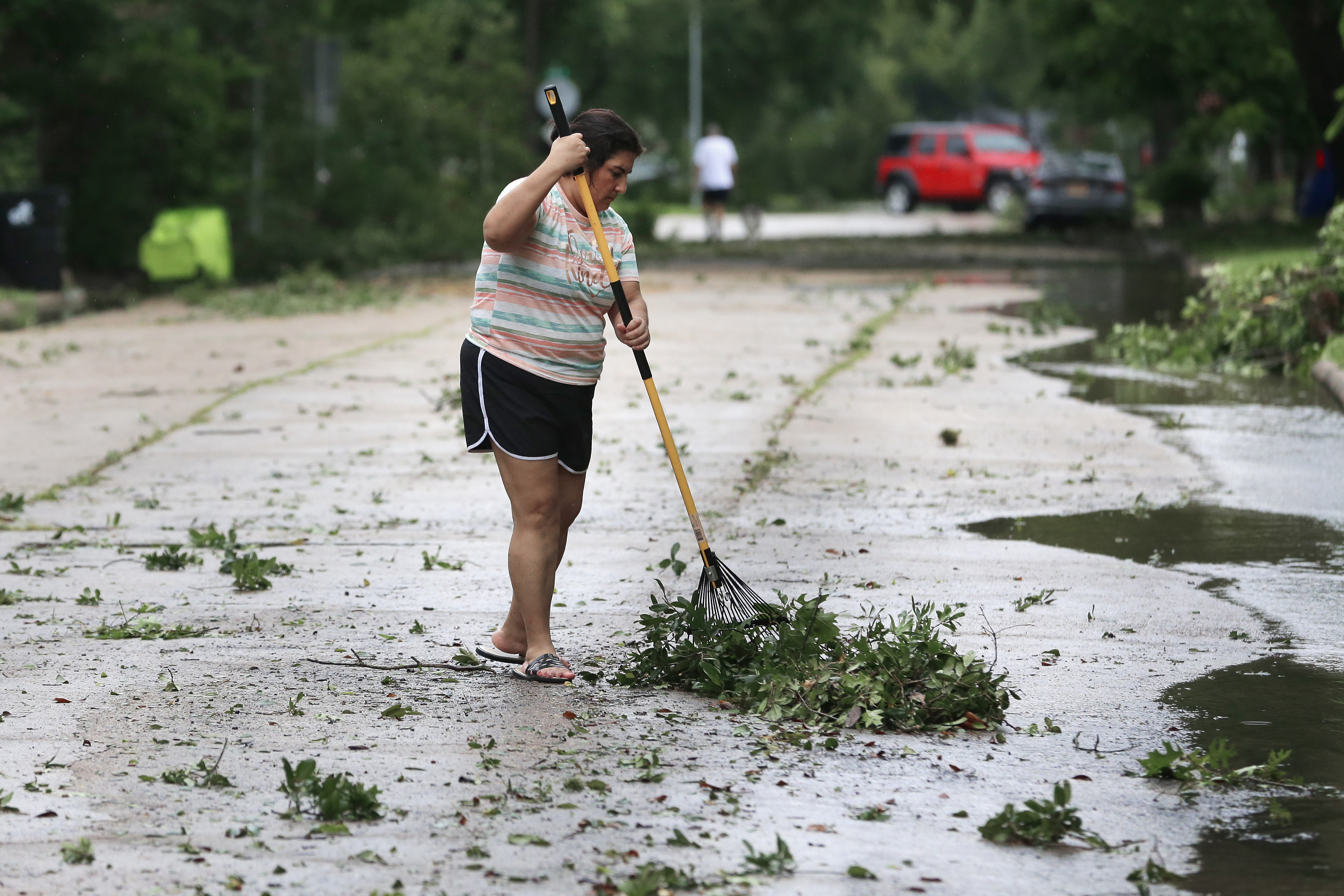 Resident Isabel Perez rakes up downed tree branches from the street outside of her home during a lull in the wind and rain as Tropical Storm Beryl passes Monday, July 8, 2024, in Rosenburg, Texas. Hurricane Beryl has been downgraded to a tropical storm after sweeping into Texas as a Category 1 storm with heavy rains and powerful winds. (AP Photo/Michael Wyke)