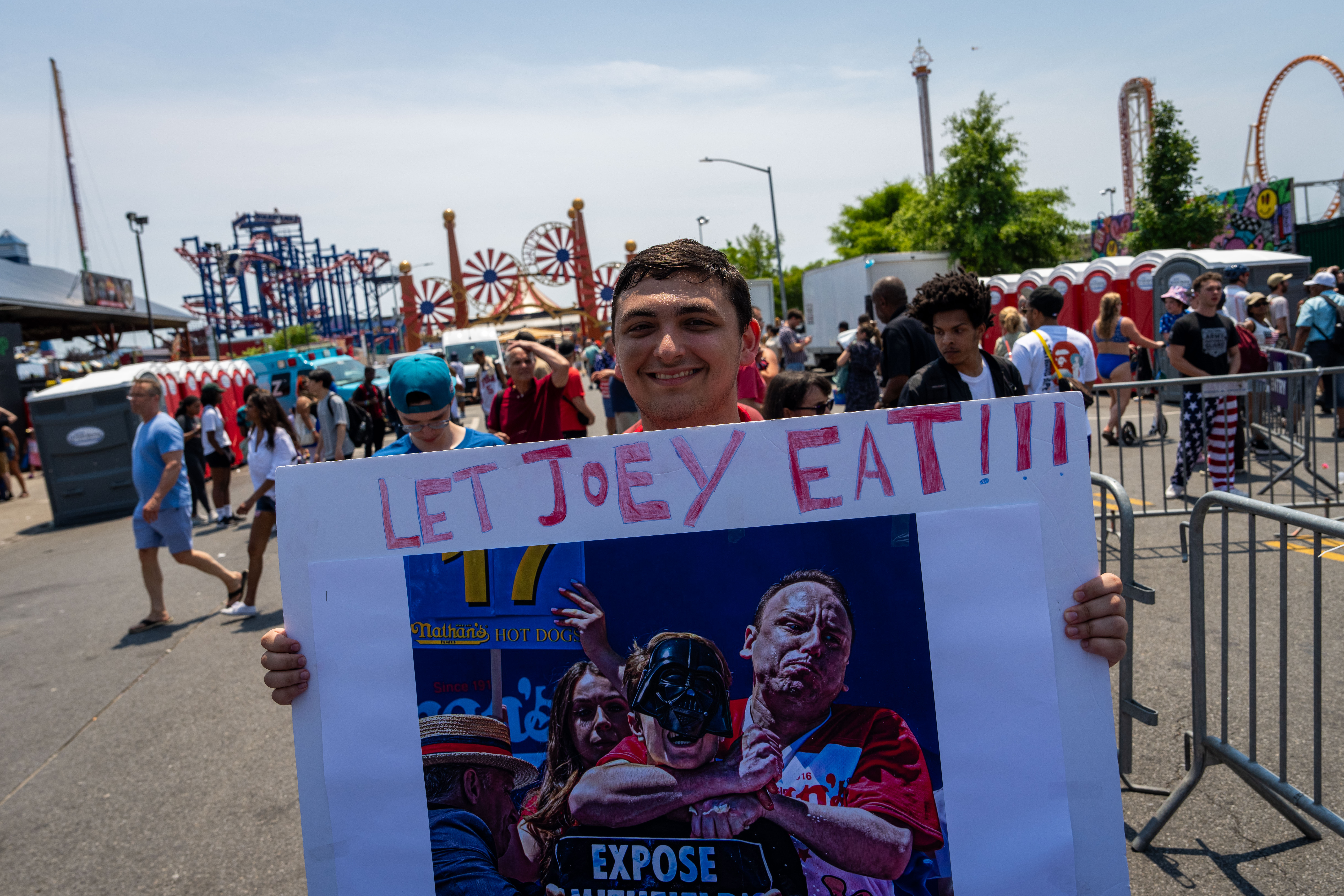 NEW YORK, NEW YORK - JULY 4: A person holds a sign saying 'Let Joey Eat' at Nathan's Annual Hot Dog Eating Contest on July 4, 2024 in New York City. Sixteen-time winner Joey Chestnut is banned from this year's contest due to his partnership with Nathan's competitor Impossible Foods, which sells plant-based hot dogs. (Photo by Adam Gray/Getty Images)