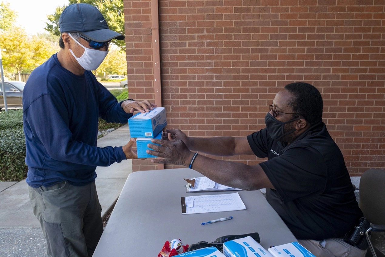 Son Chong (left) picks up free boxes of disposable masks from Kemper Williams at the Davis Police Department on Oct. 22, 2020. A ballot initiative that would have raised taxes on California millionaires and billionaires to fund public health programs and pandemic prevention has stalled. (ALIE SKOWRONSKI / THE SACRAMENTO BEE)