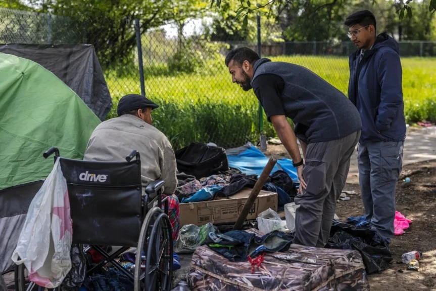 Neighborhood resource coordinators Jawid Sharifi, center, and Gustavo Tellez, right, meet with unhoused residents at a homeless encampment on W Street and Alhambra Boulevard in Sacramento on April 11, 2023. (Photo: Rahul Lal/CalMatters)