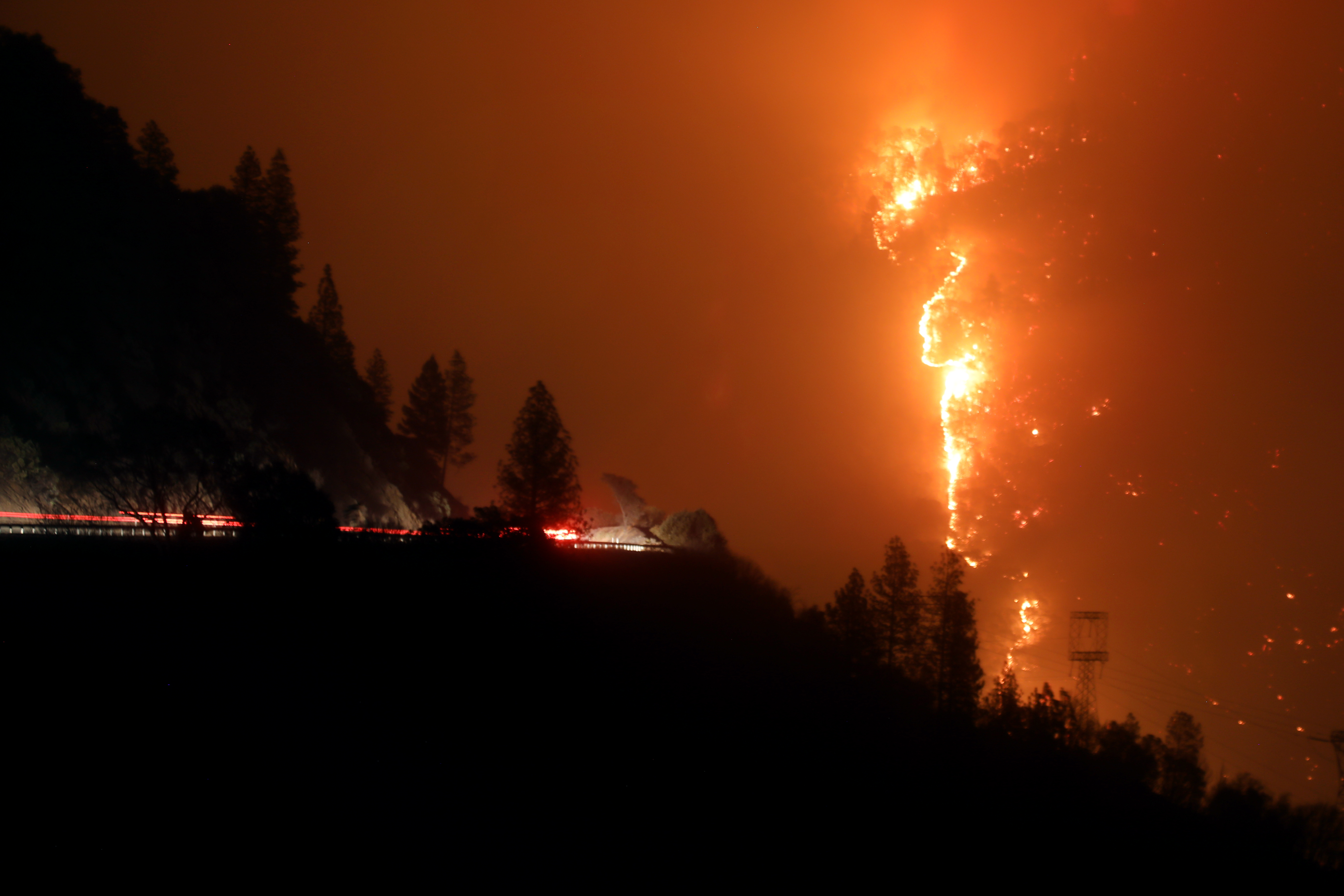 Firefighters drive toward the Camp Fire climbing a mountainside off Highway 70 west of Pulga, early on Nov. 11, 2018.