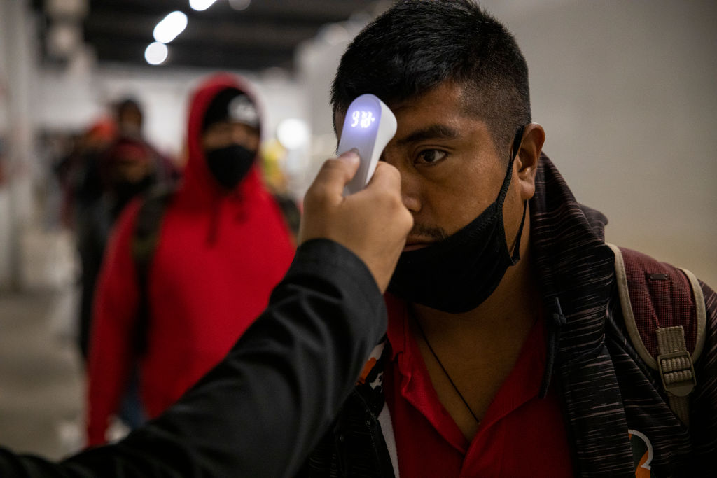 Migrant farm laborers with Fresh Harvest working with an H-2A visa have their temperature checked and are asked questions about their health before boarding the bus to their shift