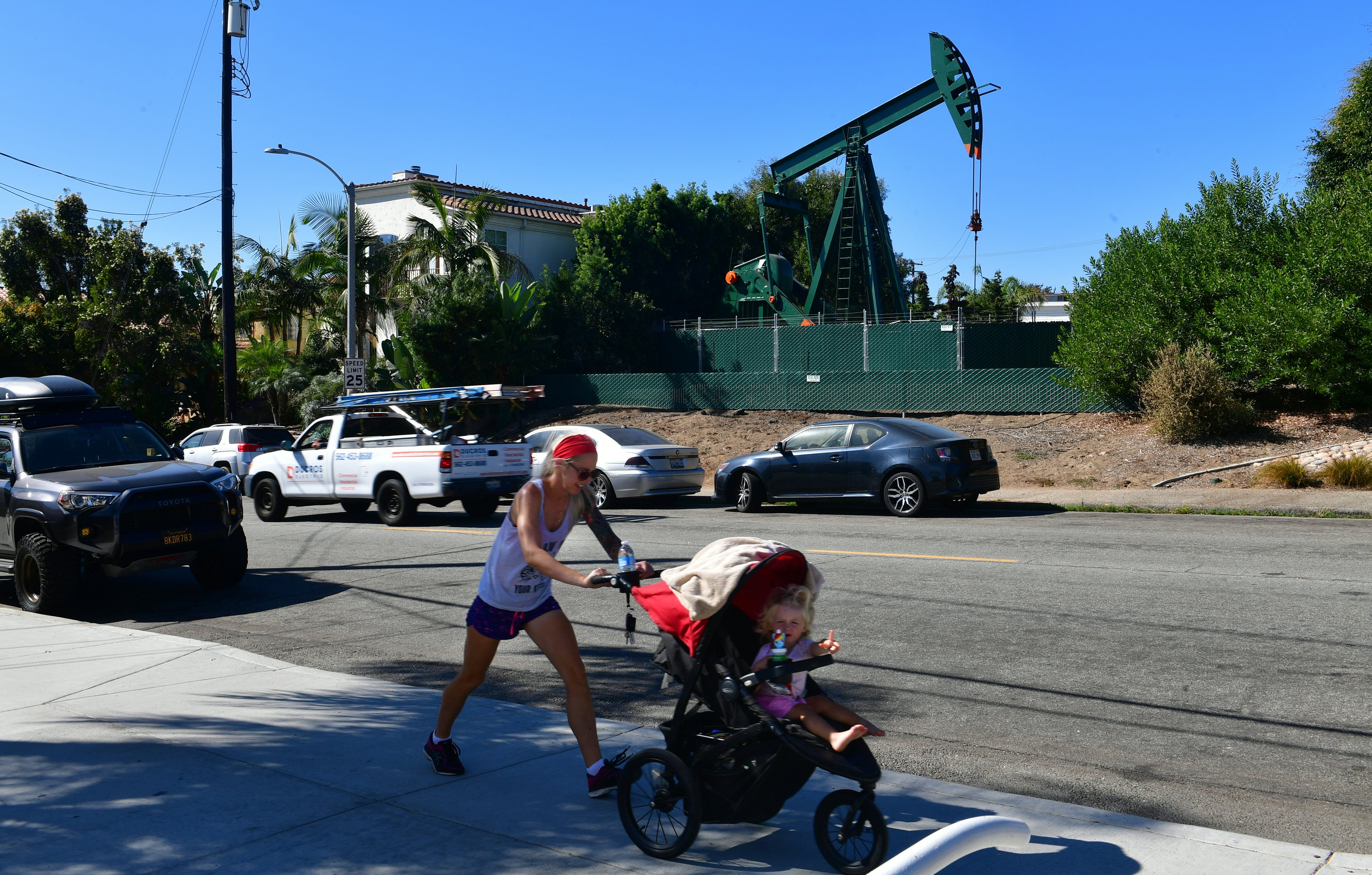 Heather Hartmann pushes her daughter Everly, 2, in a stroller past a pumpjack in an oil well on Oct. 21, 2019 in Signal Hill, south of Los Angeles