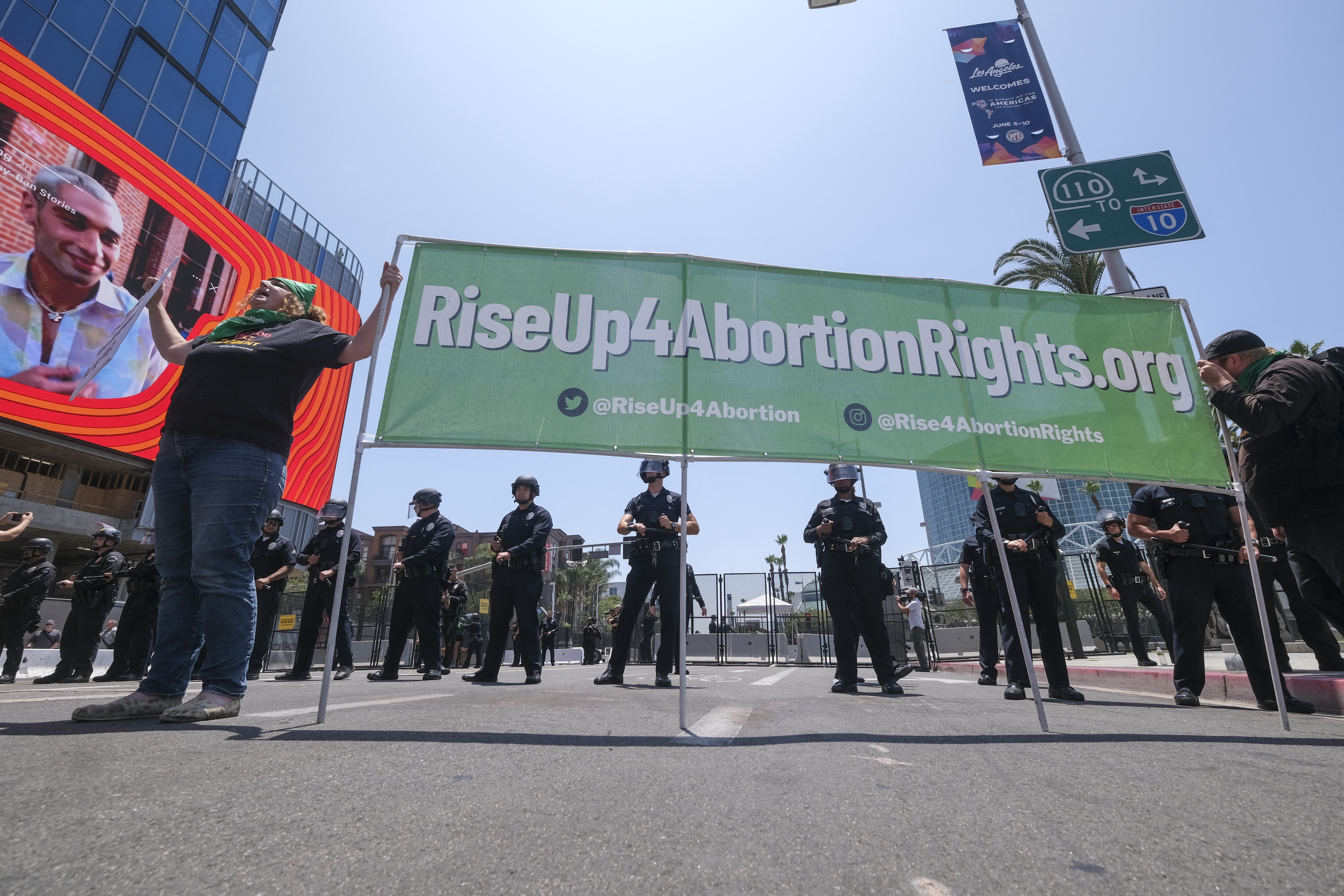 An abortion rights protester stands by a banner as police officers clear the street during a protest outside the Convention Center where the 9th Summit of the Americas takes place in Los Angeles, Calif., June 9, 2022.