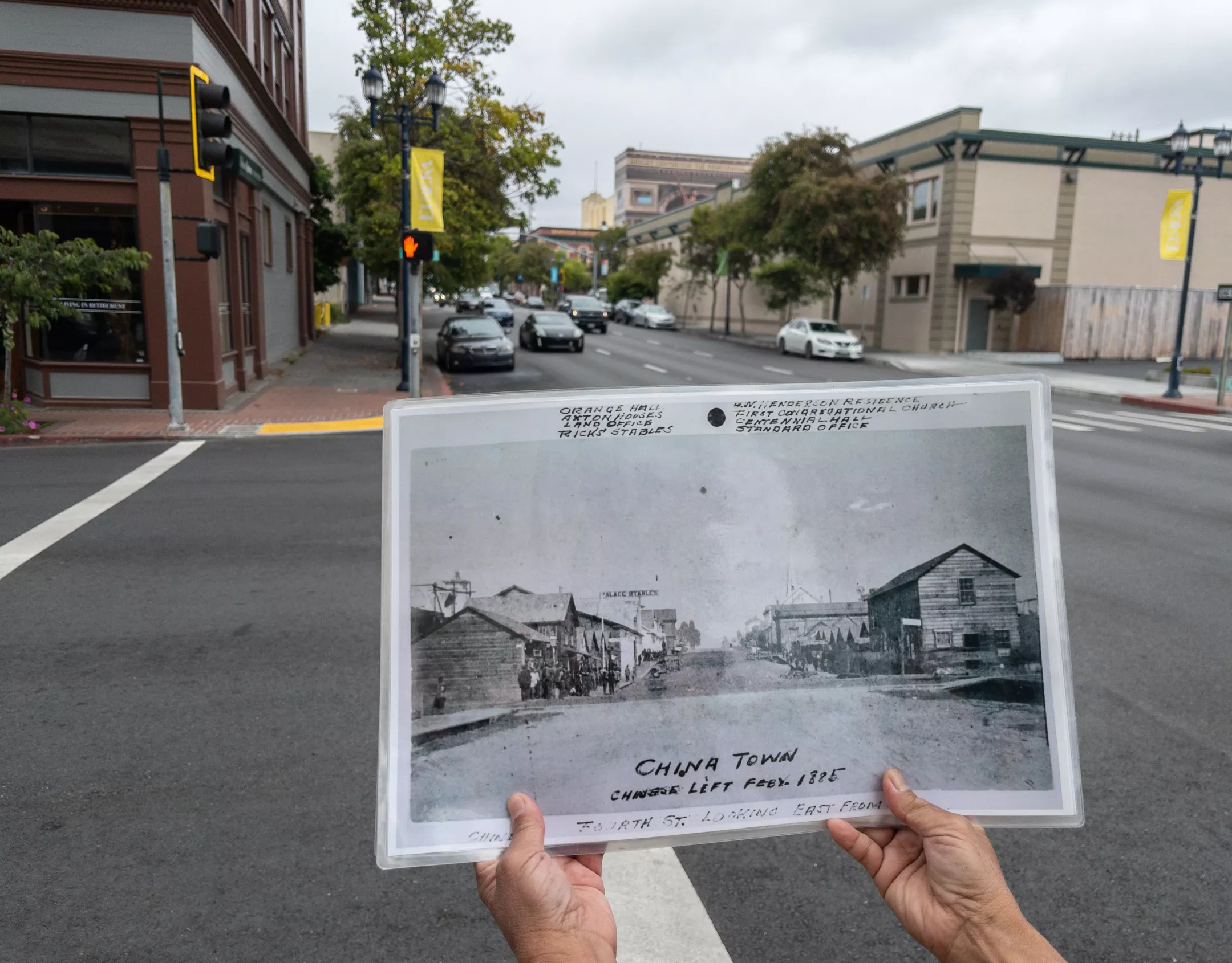 A historical photo is held up at the corner of 4th and E Streets in Eureka during a guided tour of the city's old Chinatown, which stood on the right in both images.