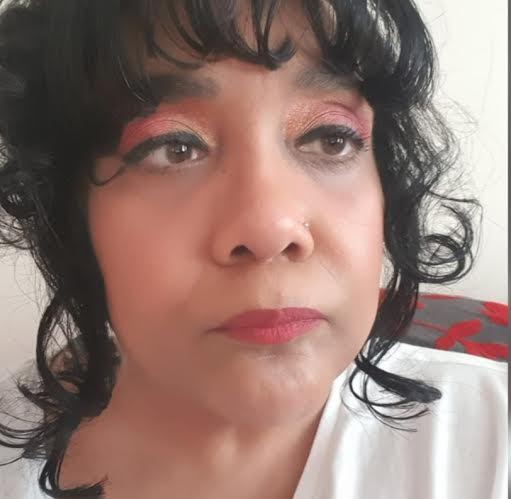 head shot of a woman of colour. She has black curly hair and eye make up on.