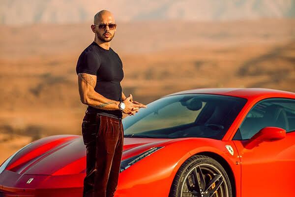 Andrew Tate standing by his red sports car