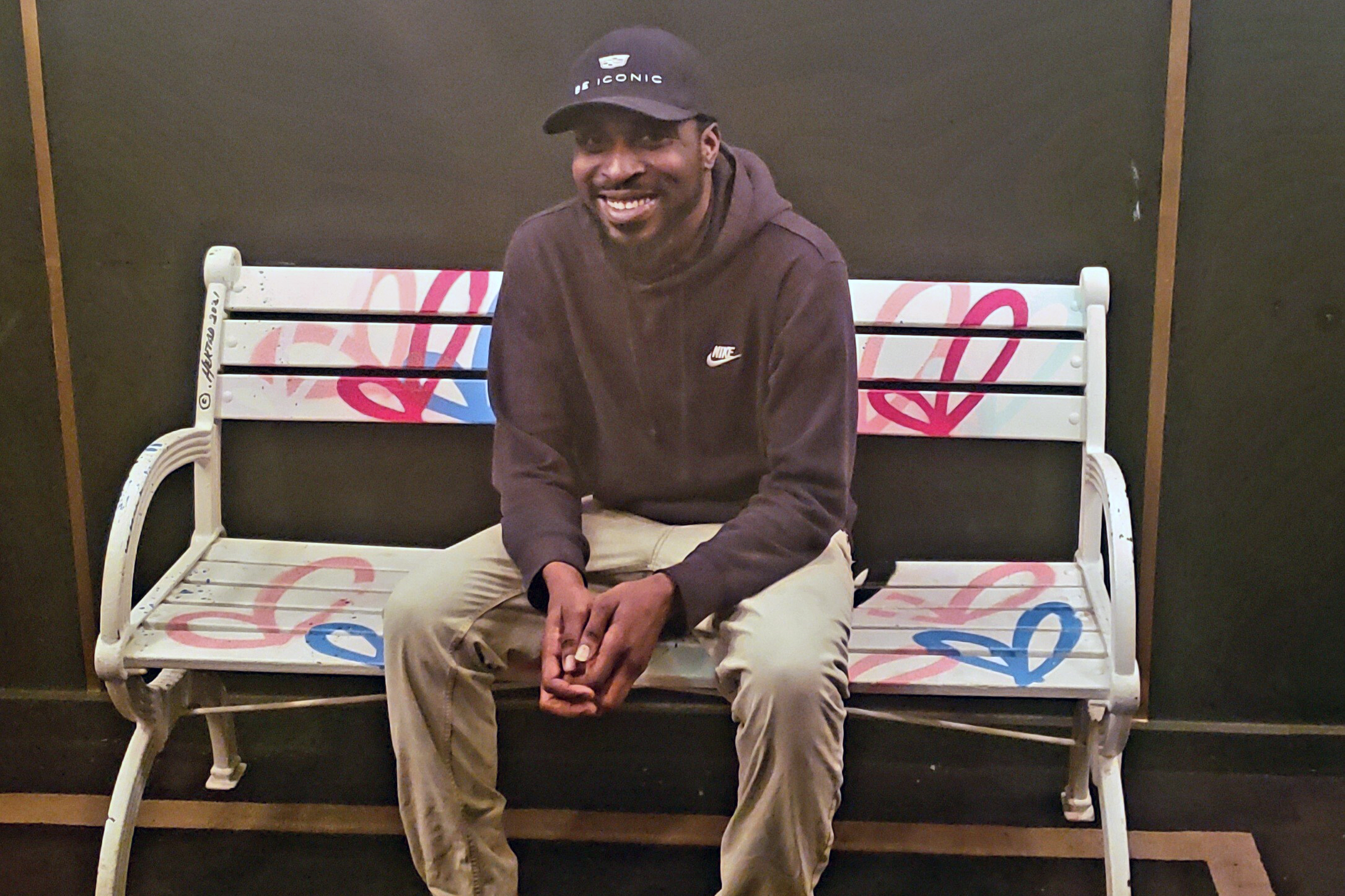 Jumal George smiles while sitting on a painted bench.