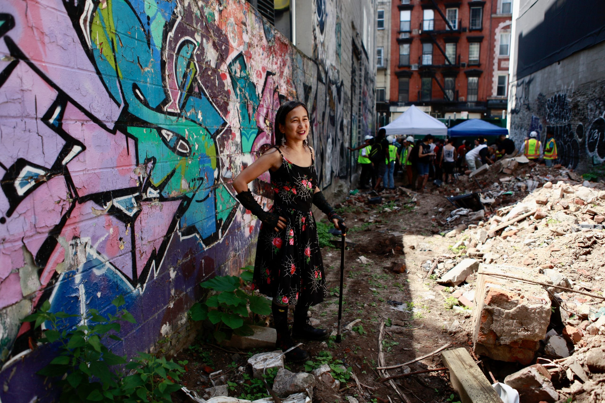 Victoria Law stands in the rubble of the former ABC No Rio with construction team and ABC community in the background. Law is the founder of Books through Bars at ABC No Rio.