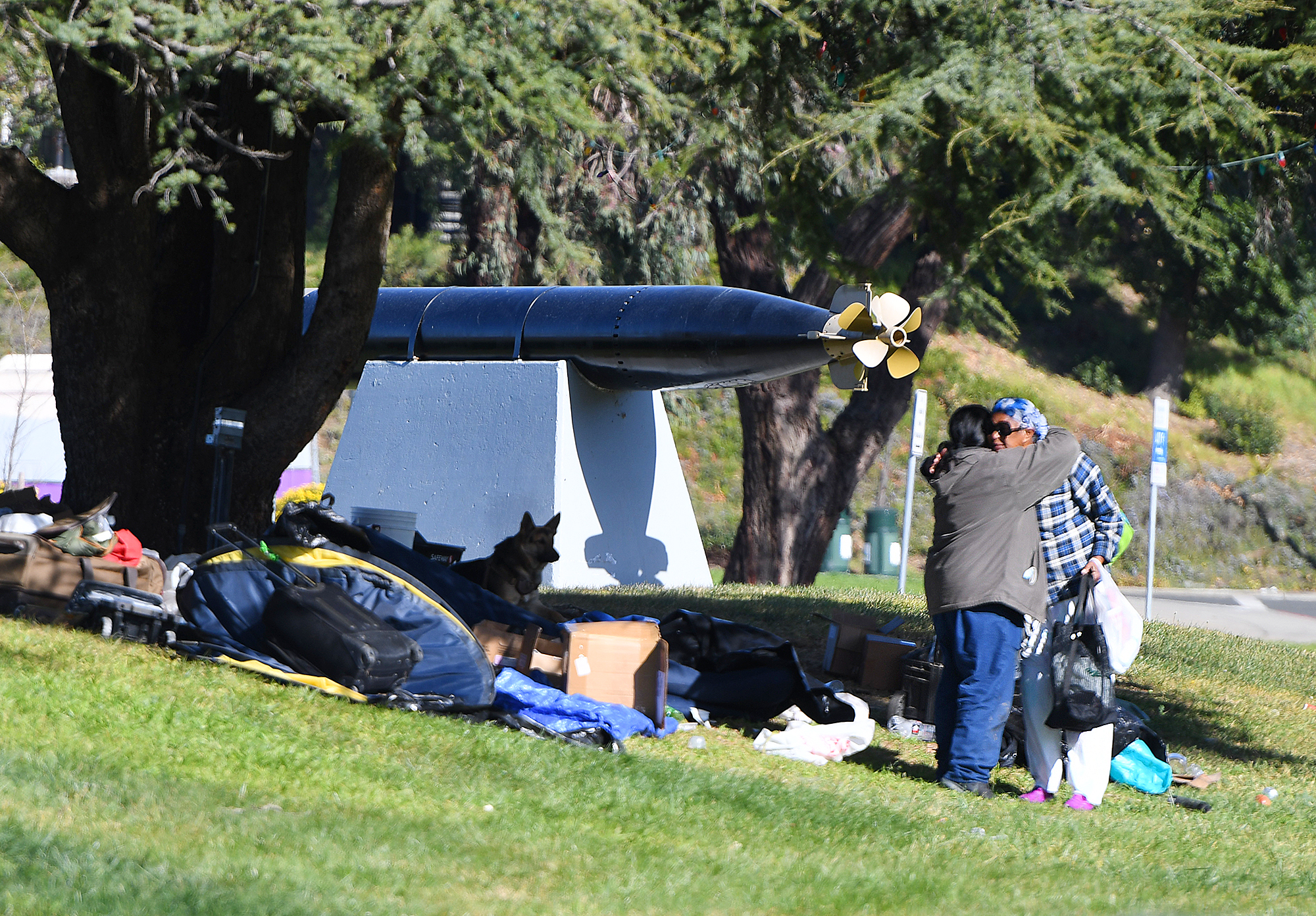 People hug as they clean up an encampment behind the JFK Library earlier this year. Homeless residents in the area were issued notices to vacate the premises. Some voluntarily left and others stayed as the city chose not to relocate anyone just yet. (Chris Riley/Times-Herald file)