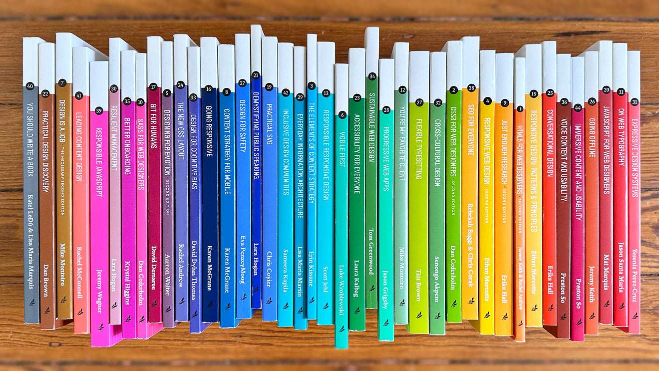 Some of A Book Apart’s 50-odd primary paperbacks, arranged like a color spectrum, and photographed against a piece of wood.