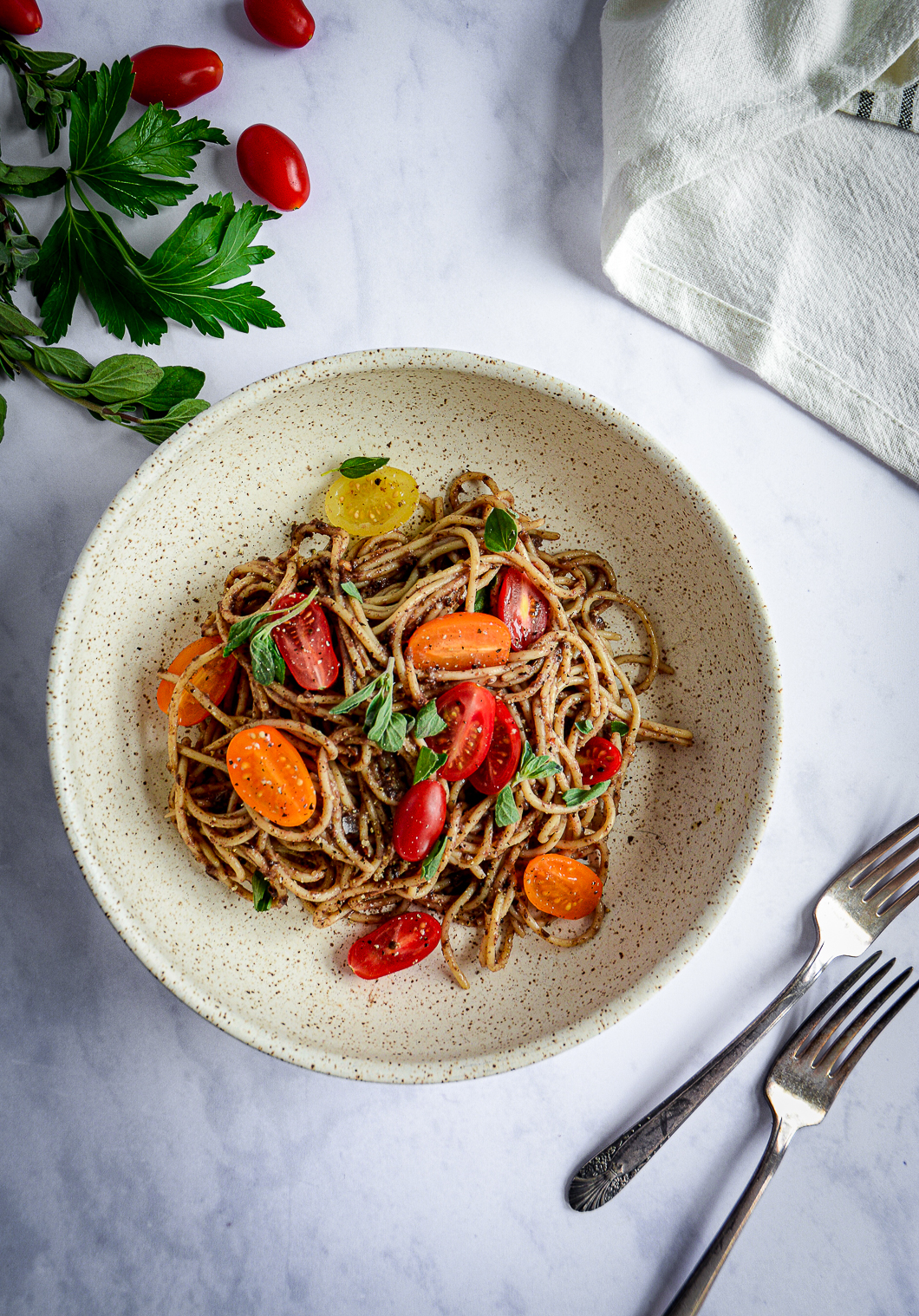 Moroccan Tapenade Spaghetti with Tomatoes and Herbs in bowl with herbs and tomatoes and forks