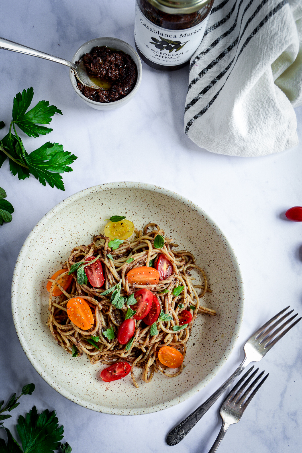 Moroccan Tapenade Spaghetti with Tomatoes and Herbs in bowl with napkin, bowl of tapenade and forks
