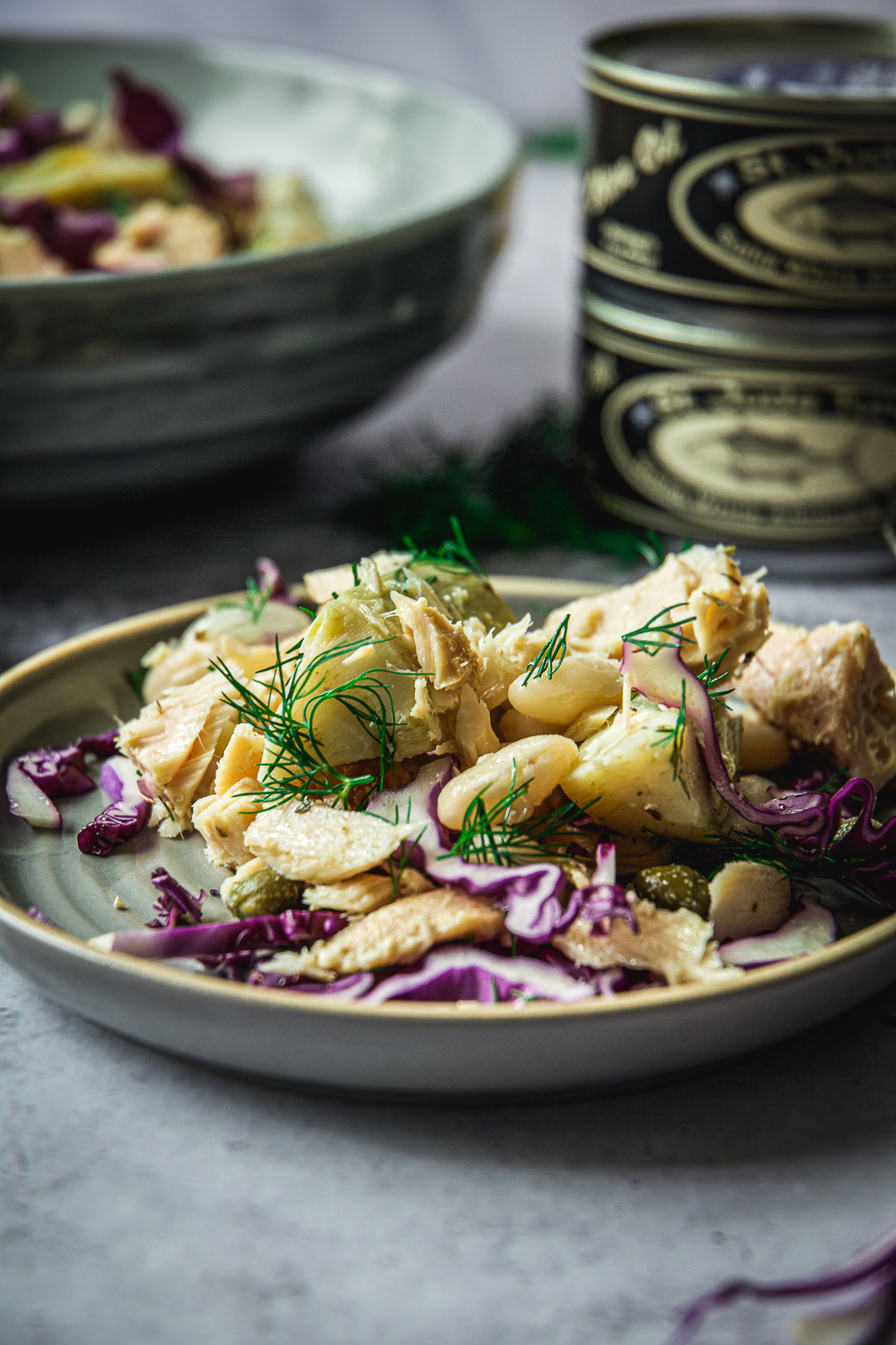 White Bean Tuna Salad with Artichoke Hearts on small plate with cans of tuna in the background 