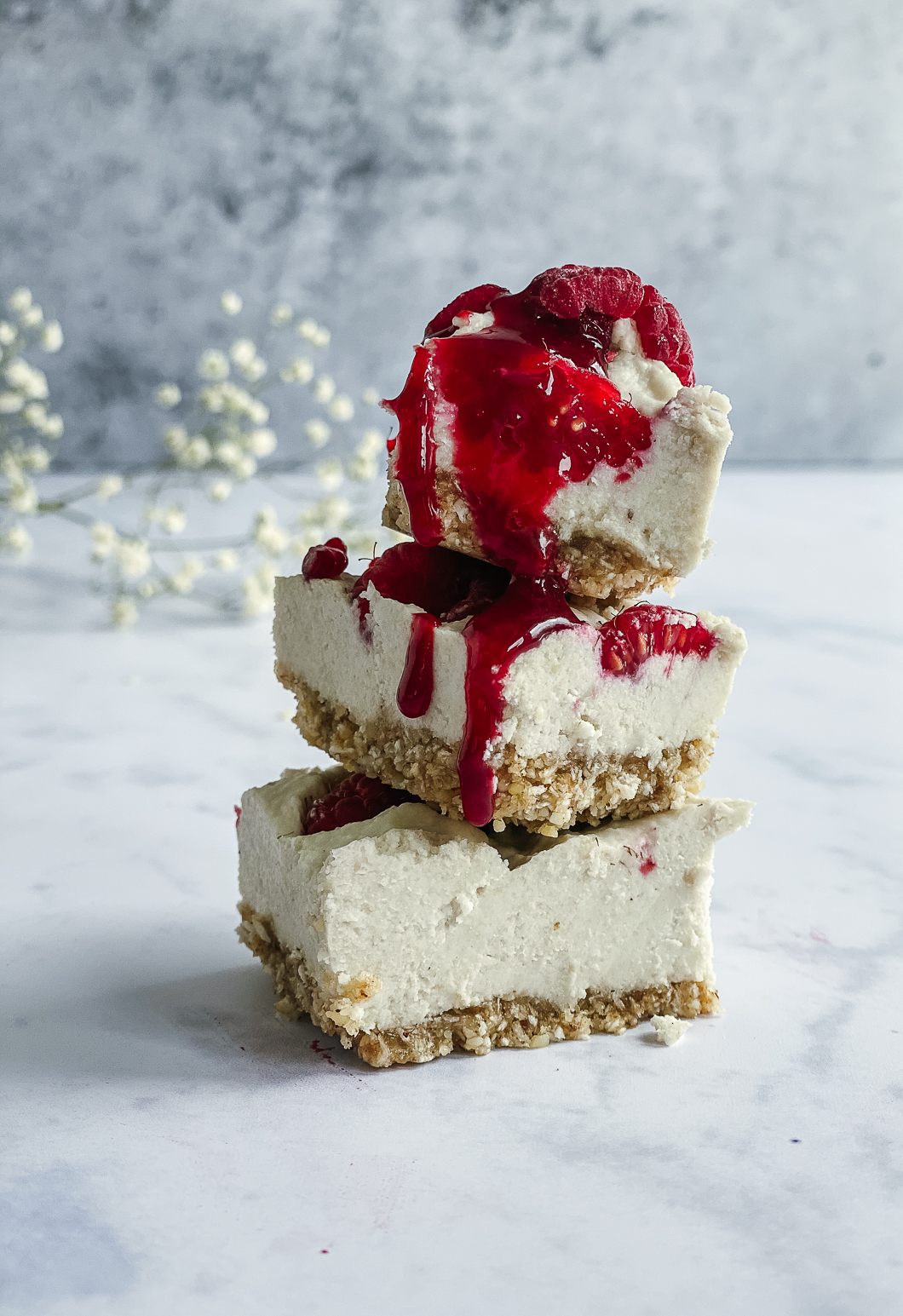 Stacked raspberry cheesecake bites drizzled with raspberry sauce