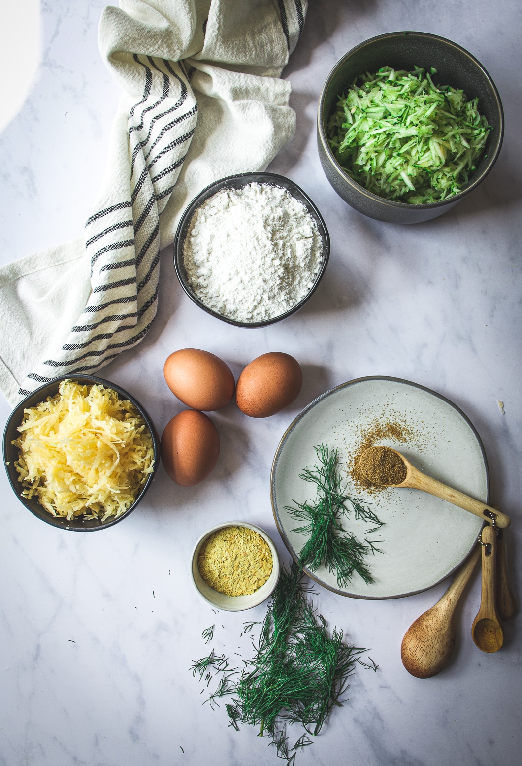 Eggs, grated rutabaga and zucchini, cassava flour, cumin on spoon and nutritional yeast on table
