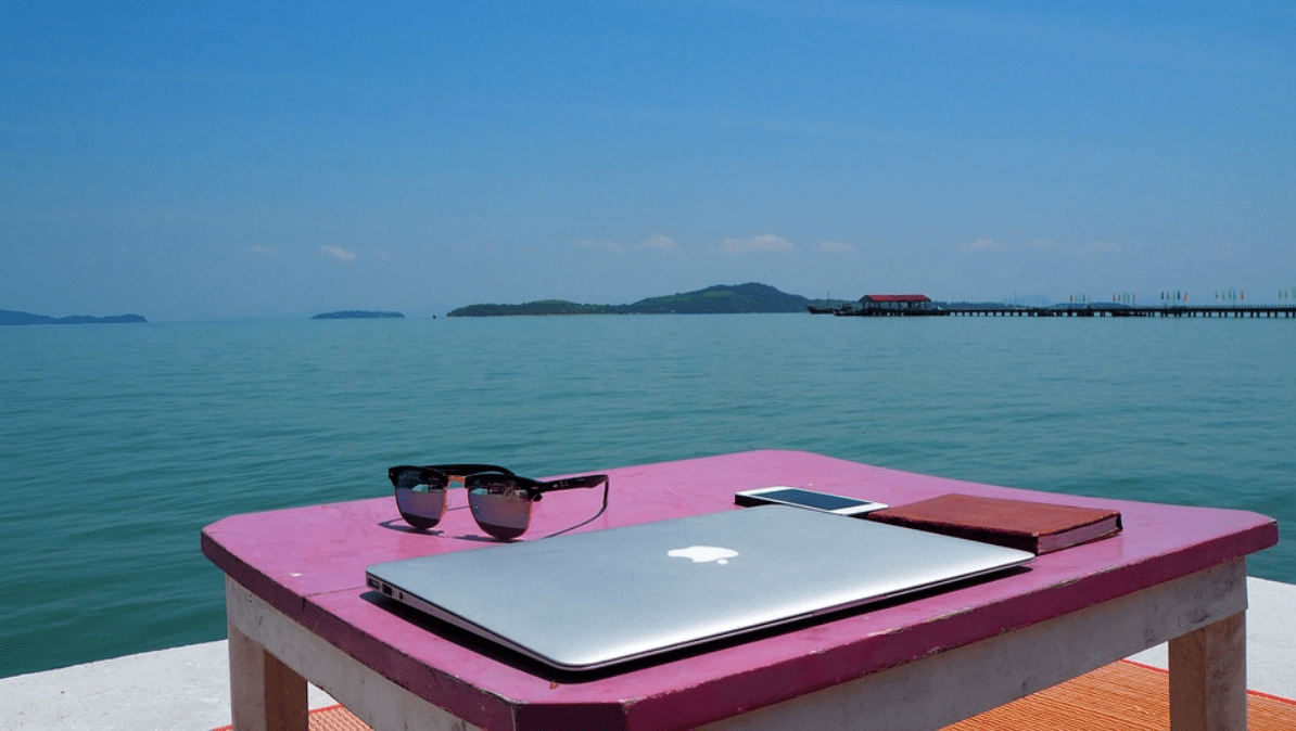 A lap top on a pink table overlooking the ocean.