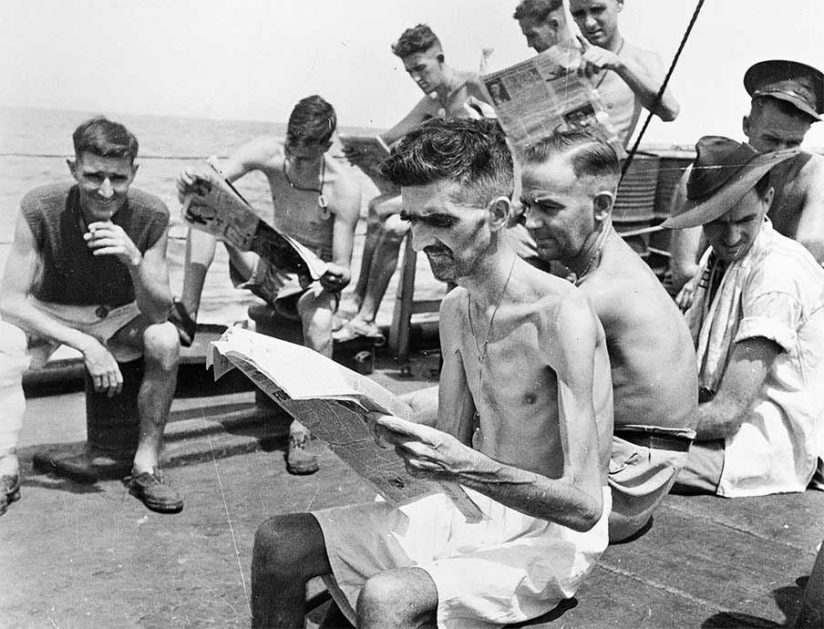 Shown to the right is a photo of men, with Private Leo Ayres in the foreground, newly liberated from the Japanese camps who were reading the newspapers about the war having just ended.