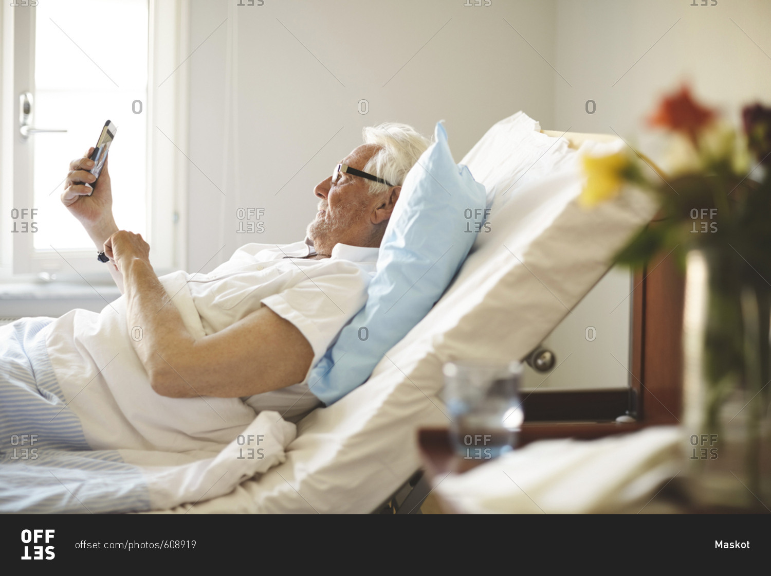 Senior man taking selfie with smart phone on bed in hospital ward stock
