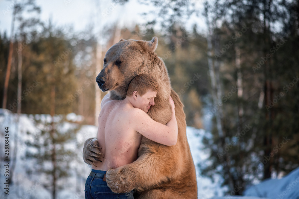 Halfnaked man hugs a brown bear in a winter forest. Bear hugs man in
