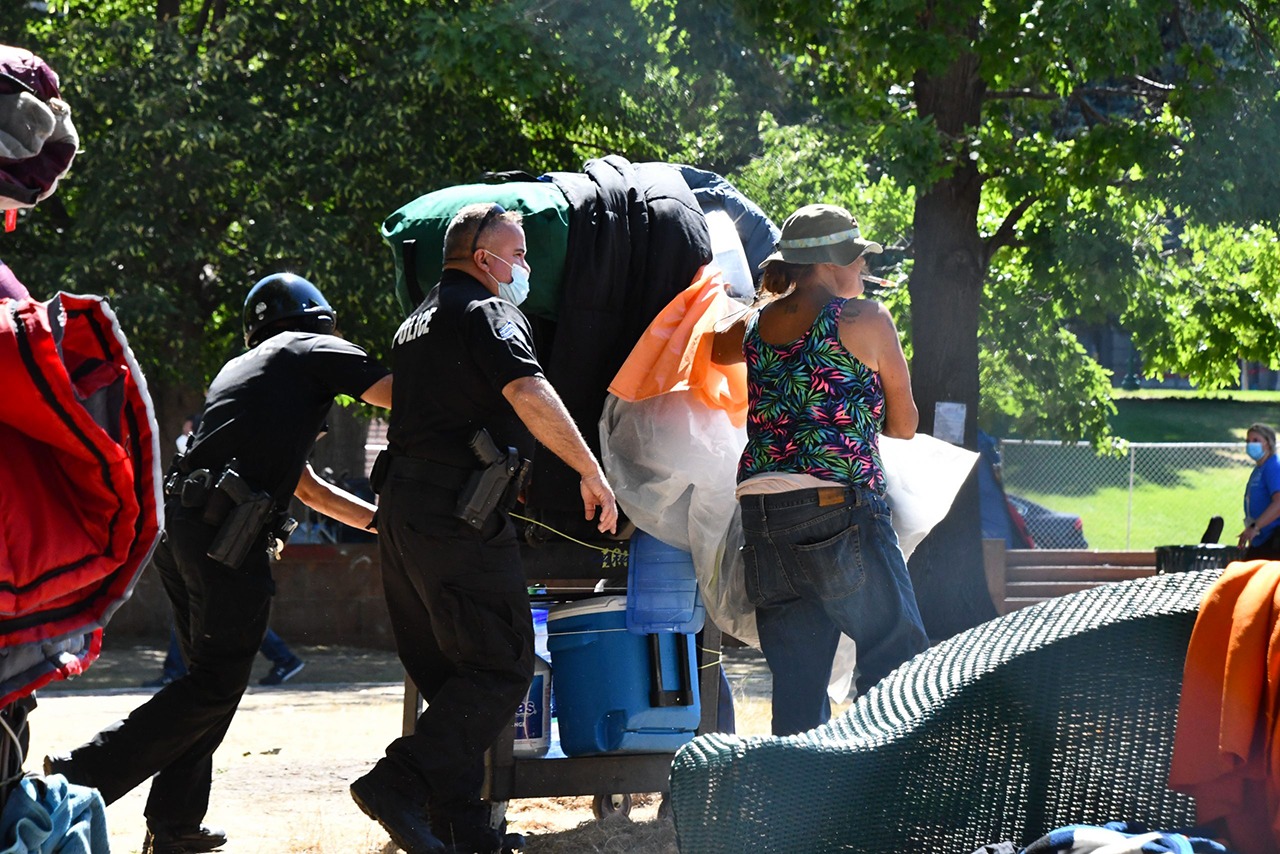 Denver police officers help a woman move her belongings out of Lincoln Park onto the sidewalk on July 29, 2020. (Moe Clark/Colorado Newsline)