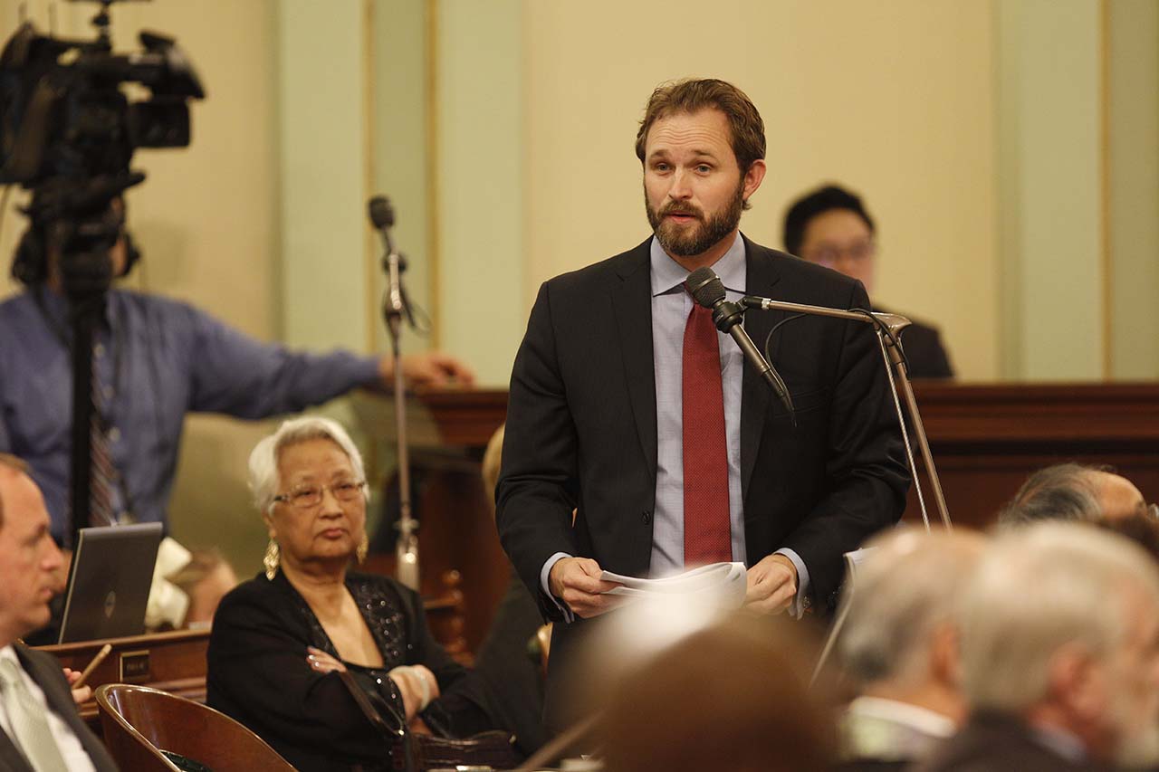 James Gallagher speaks into a microphone on the Assembly floor.