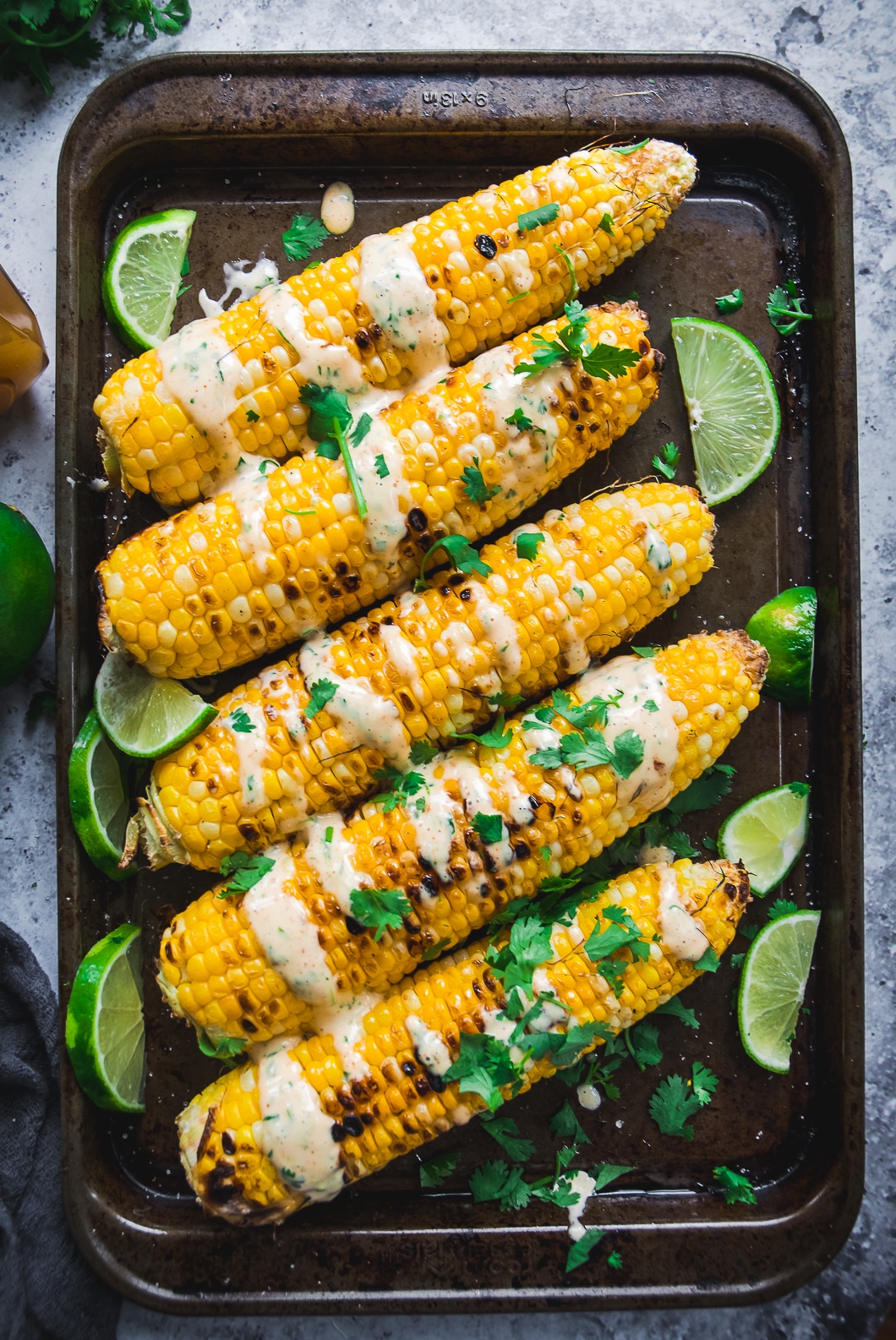 Grilled Corn with Spicy Habanero Honey Mayo on tray with lime and mayo drizzle