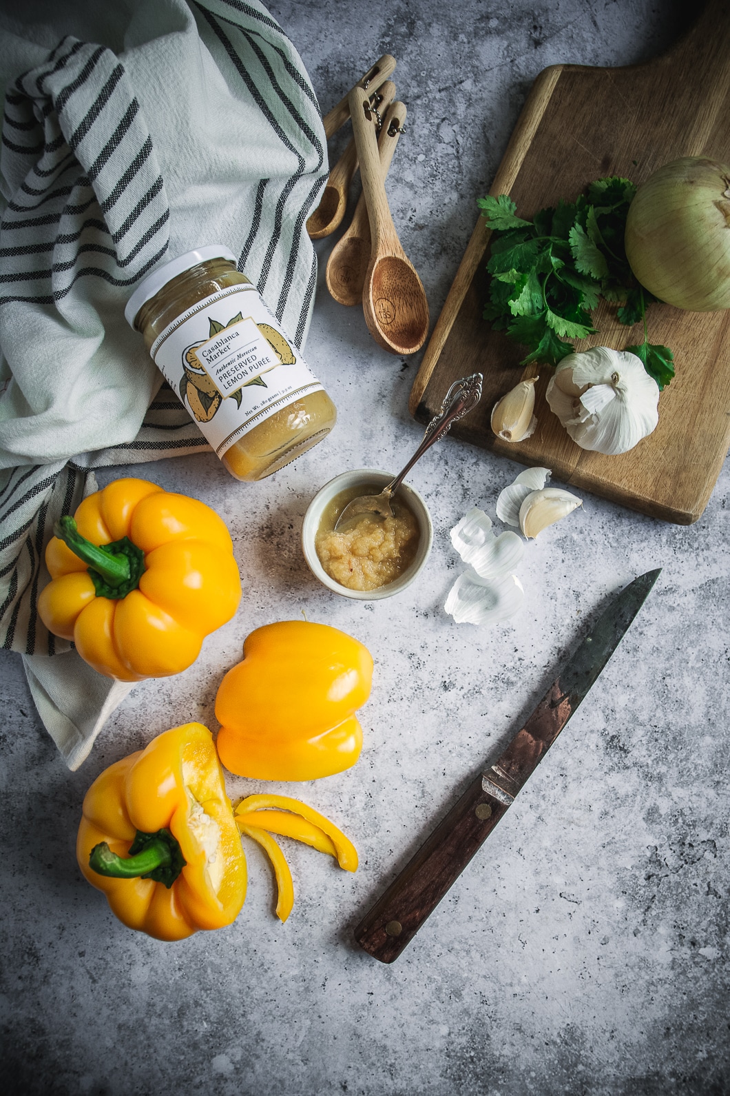Yellow peppers, onion, measuring spoons, preserved lemon puree, knife, cutting board and napkin