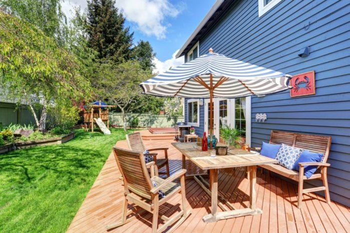 Wooden Walkout Deck In The Backyard Garden Of Blue Siding House. Home Upgrades That Add Value