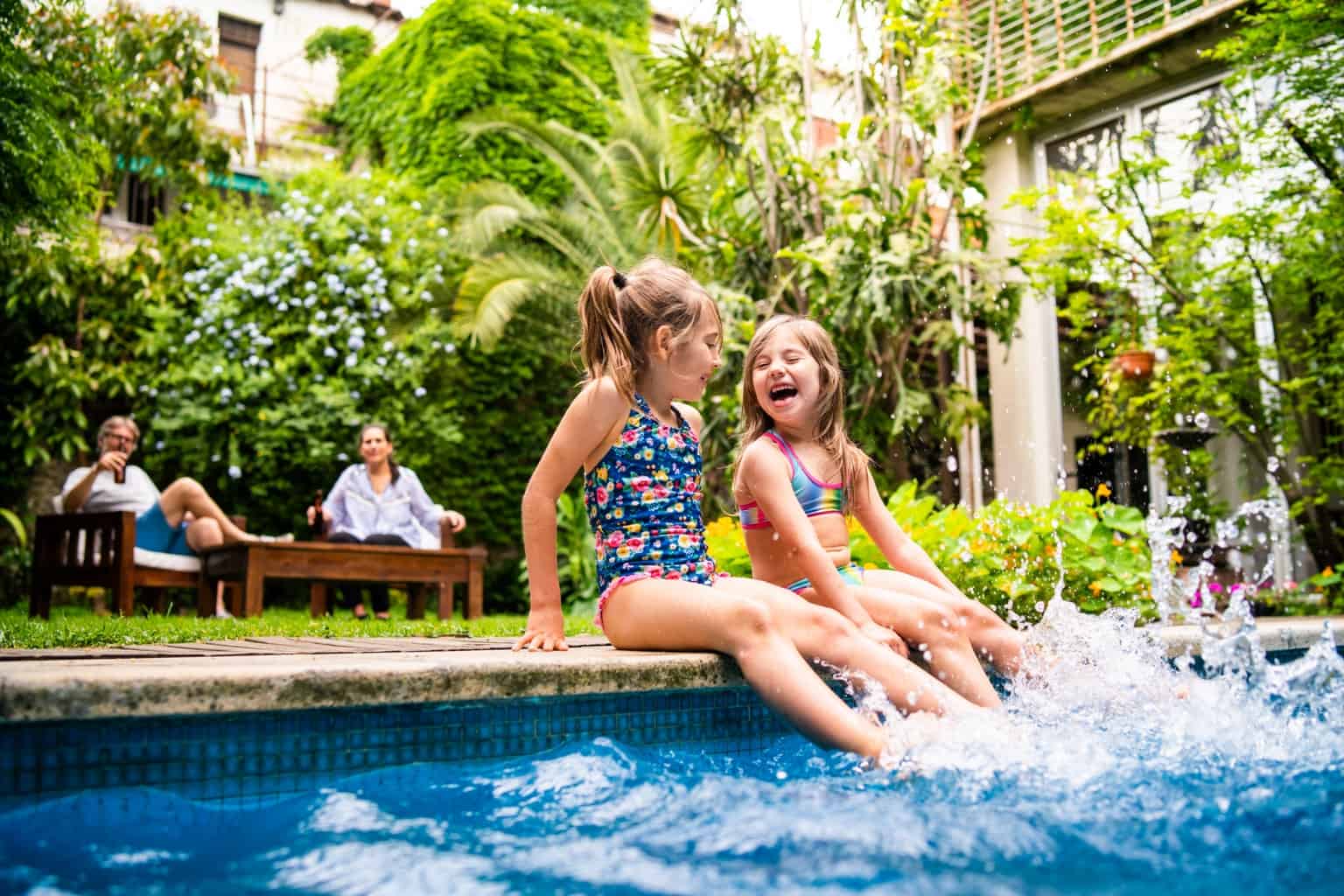 Two little girls sitting at poolside and splashing water with legs So