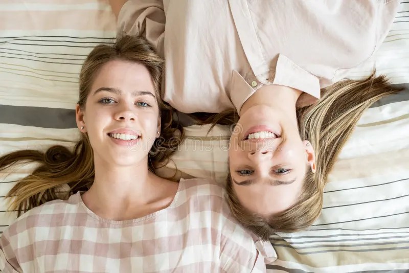 Two Cheerful Blond Teenage Girls Relaxing on Bed at Leisure Stock Image