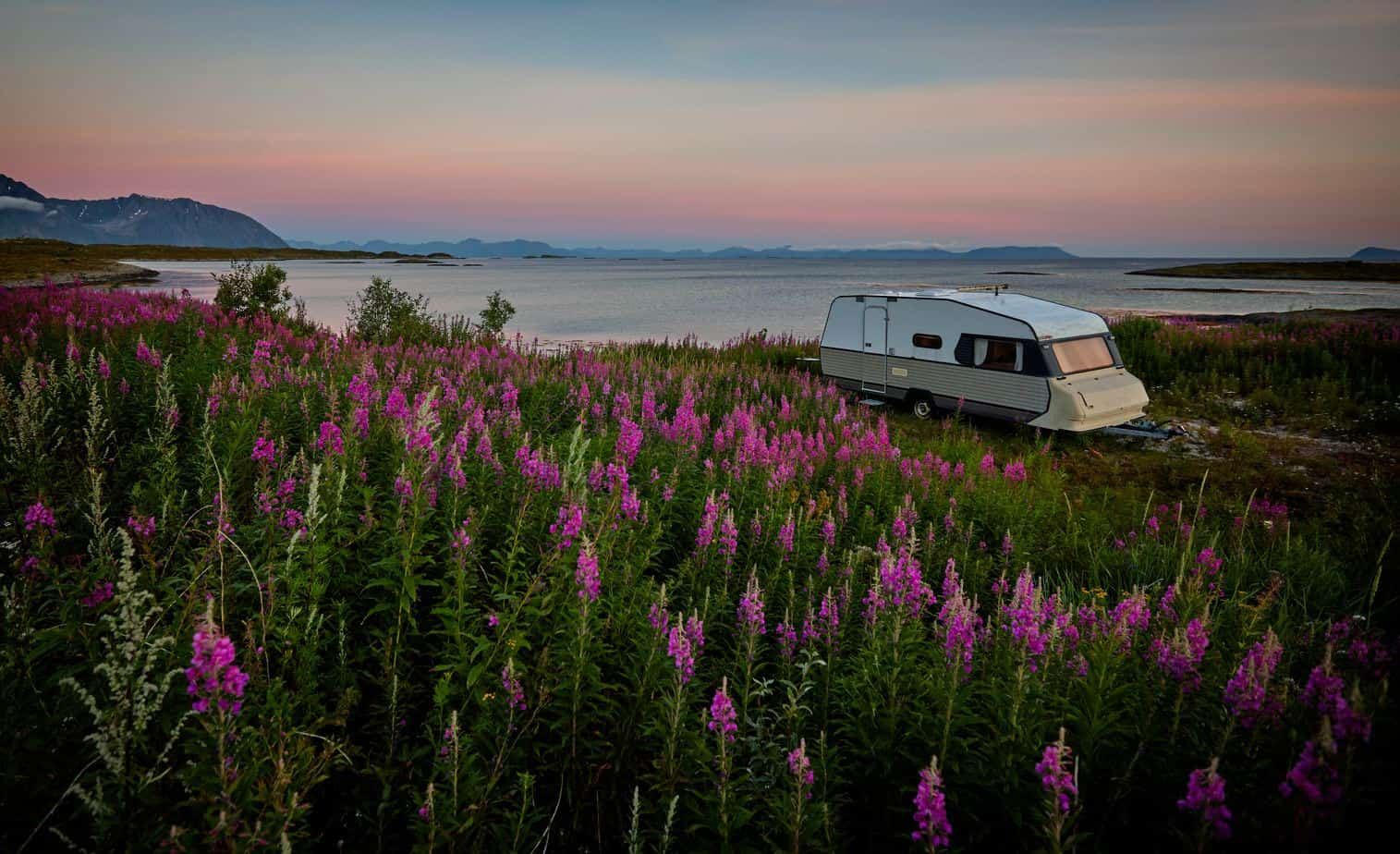 A white RV parked during sunrise in front of a lake with mountains in the background.